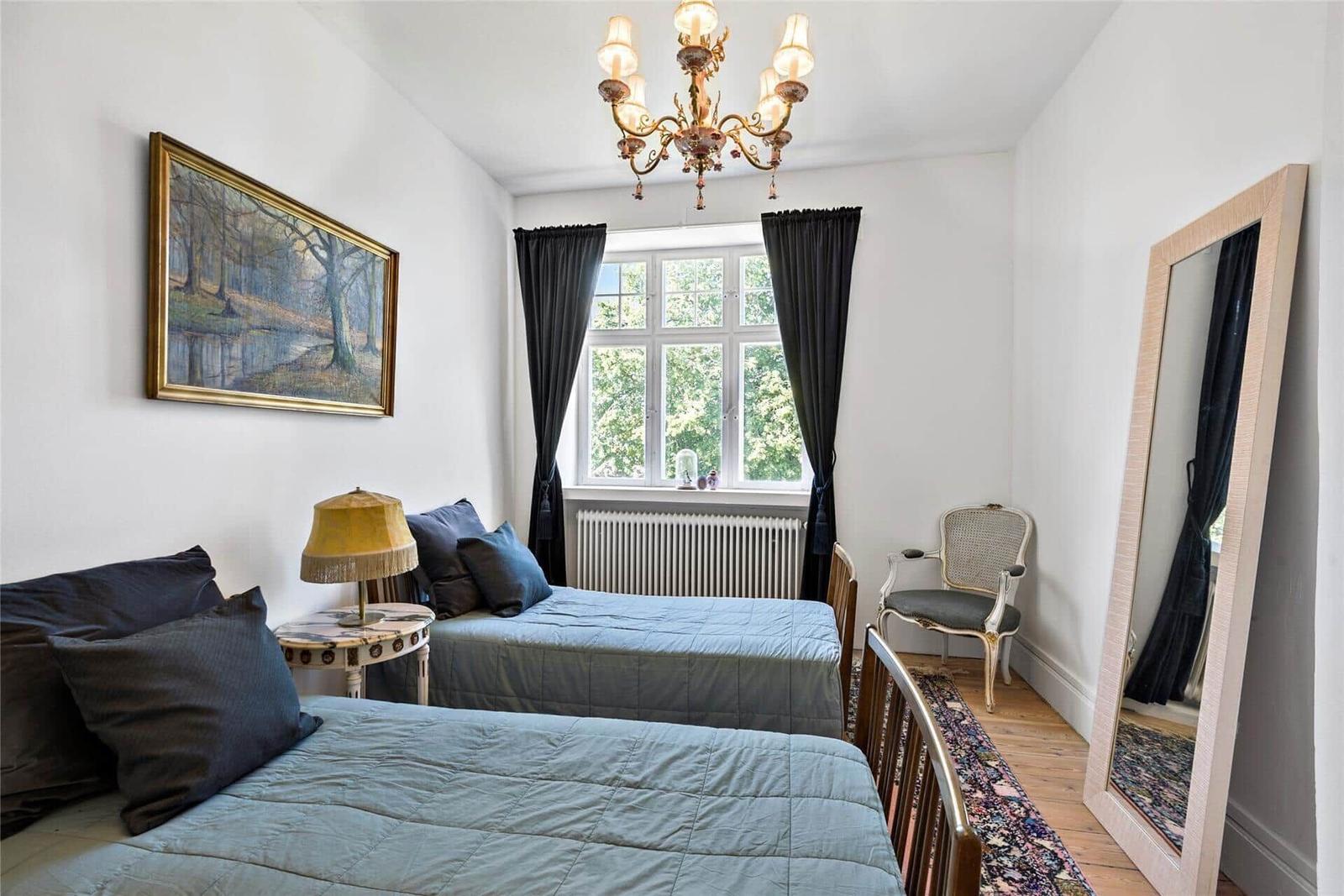 Zwei Betten, Spiegel, Stuhl und Fenster mit Vorhängen.