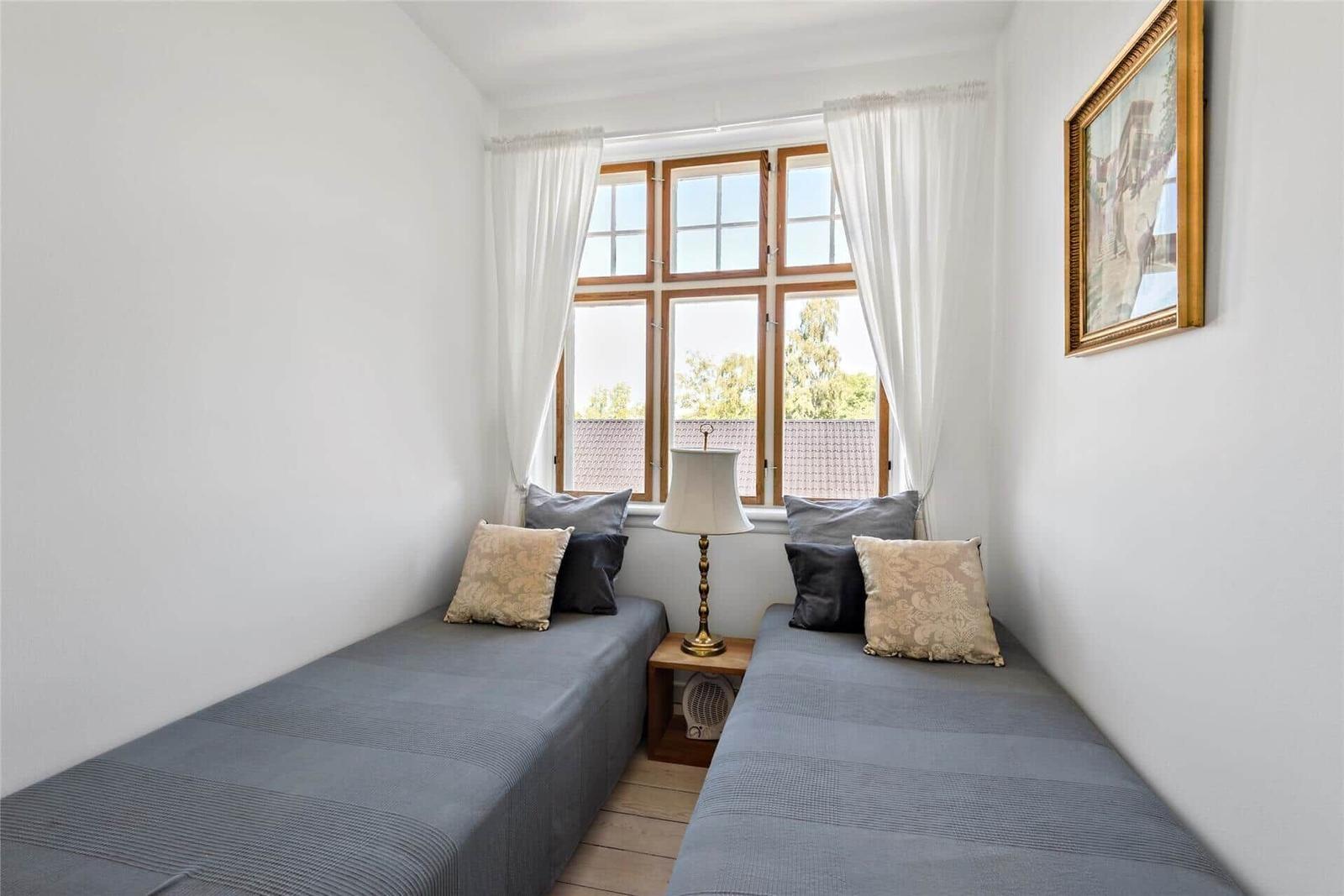 Zwei Betten mit Kissen stehen vor einem Fenster mit weißen Vorhängen.