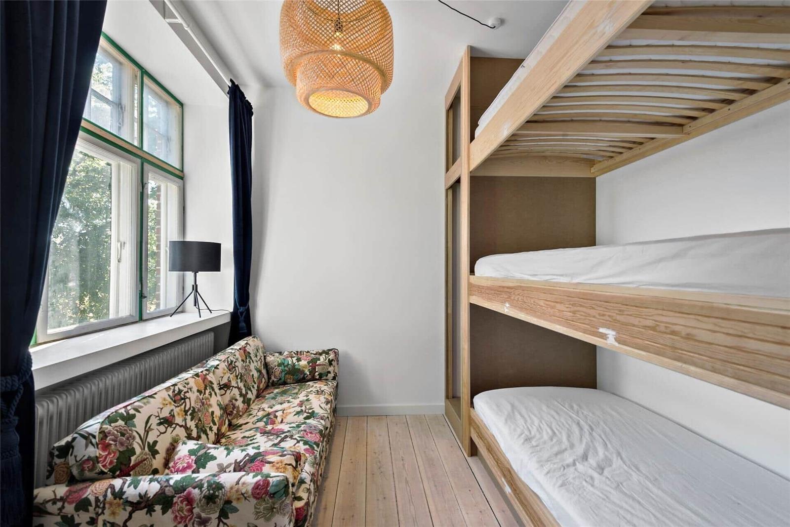Zimmer mit Schlafcouch, Doppelstockbett und Fenster mit Blick auf Grün.