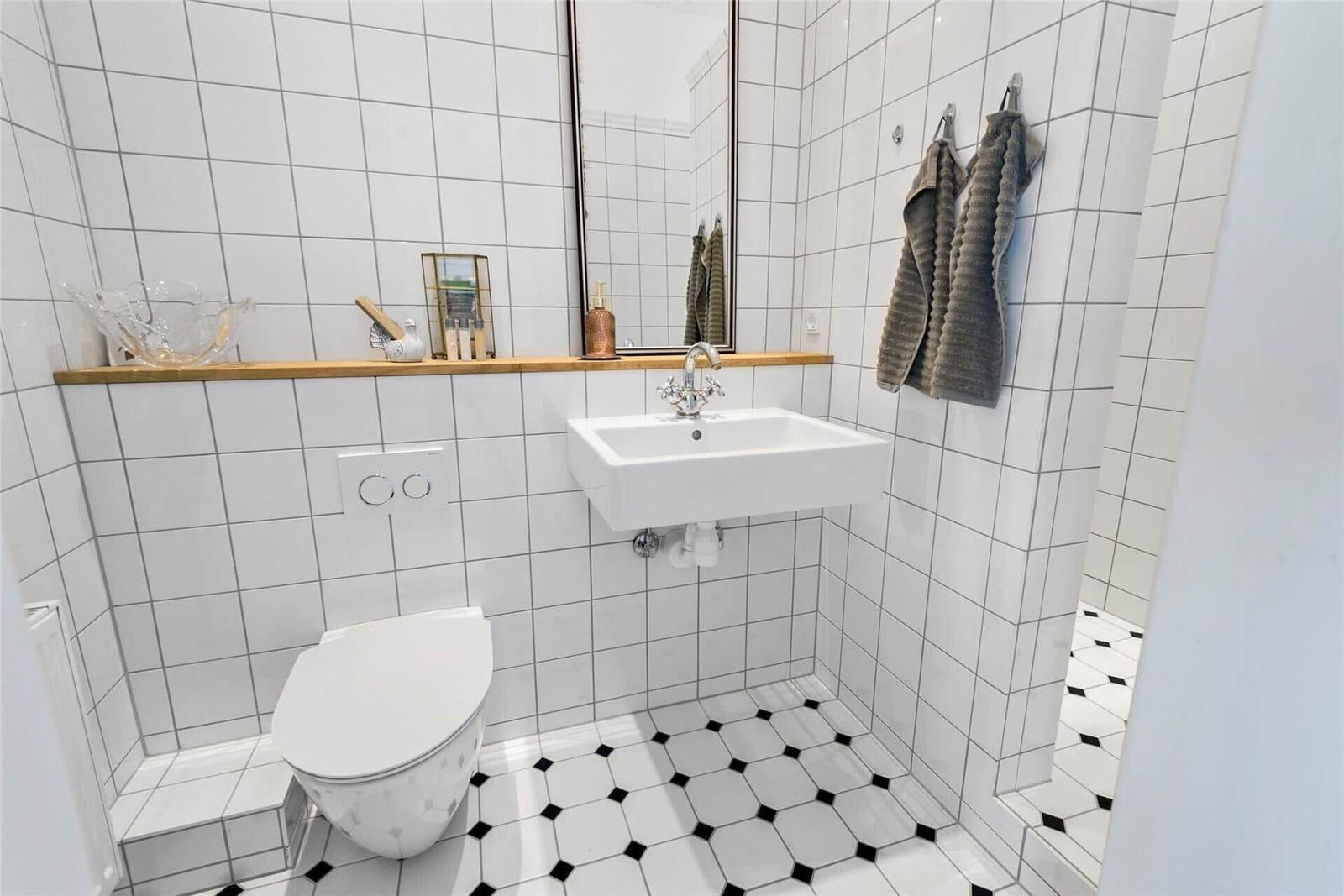 Badezimmer mit Toilette, Waschbecken und Spiegel. Fliesen an Wänden und Boden.