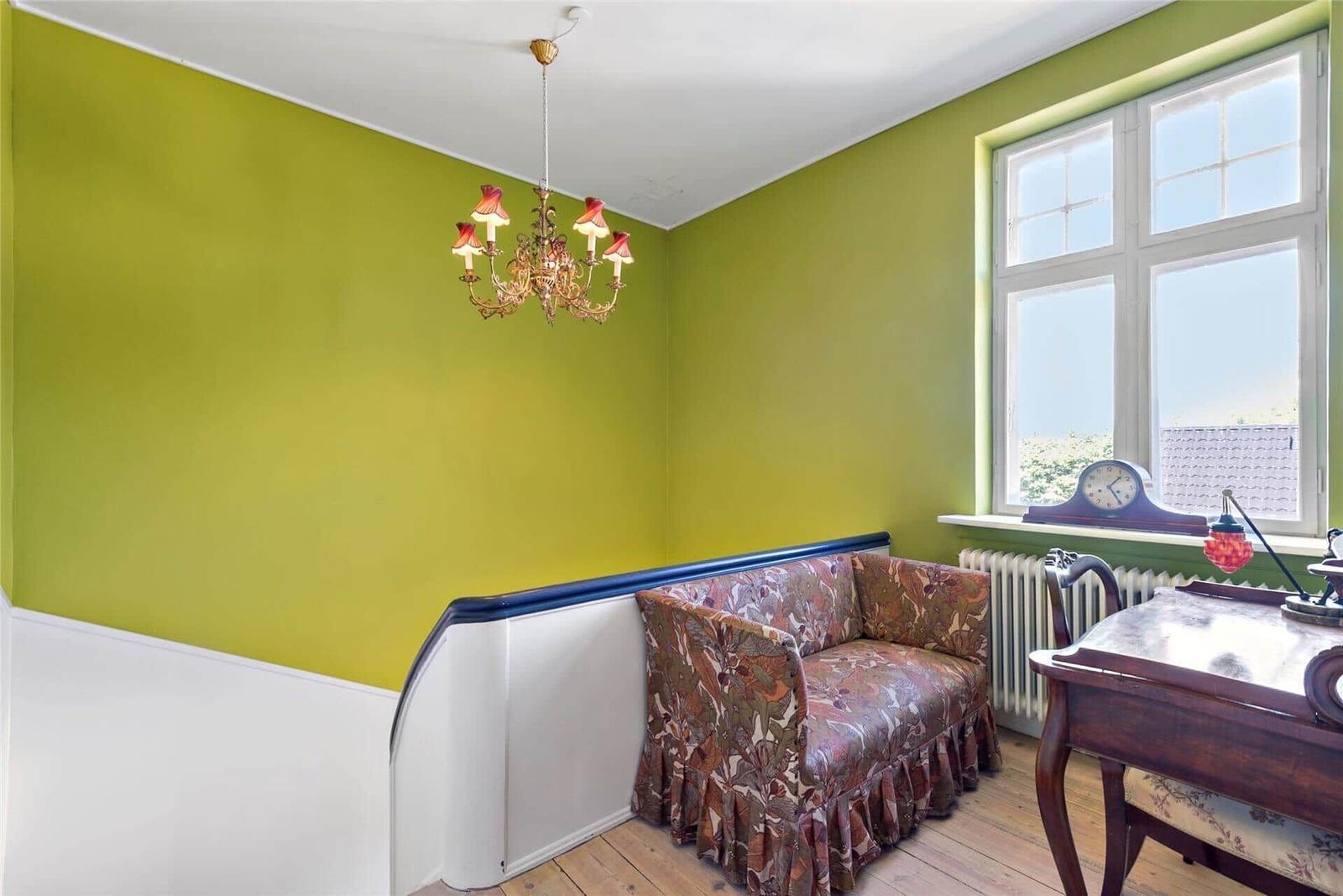 Ein Raum mit grünen Wänden, einem Sofa mit floraler Bezugsstoffe, einem Schreibtisch und einem Kronleuchter.