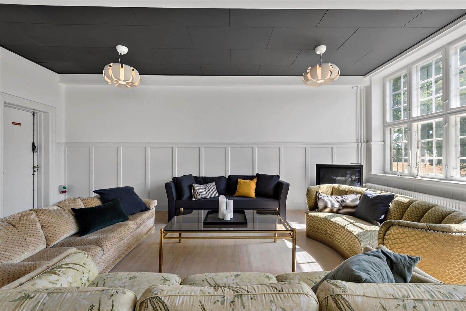 Wohnzimmer mit drei Sofas, Glas-Tisch und schwarzer Decke.