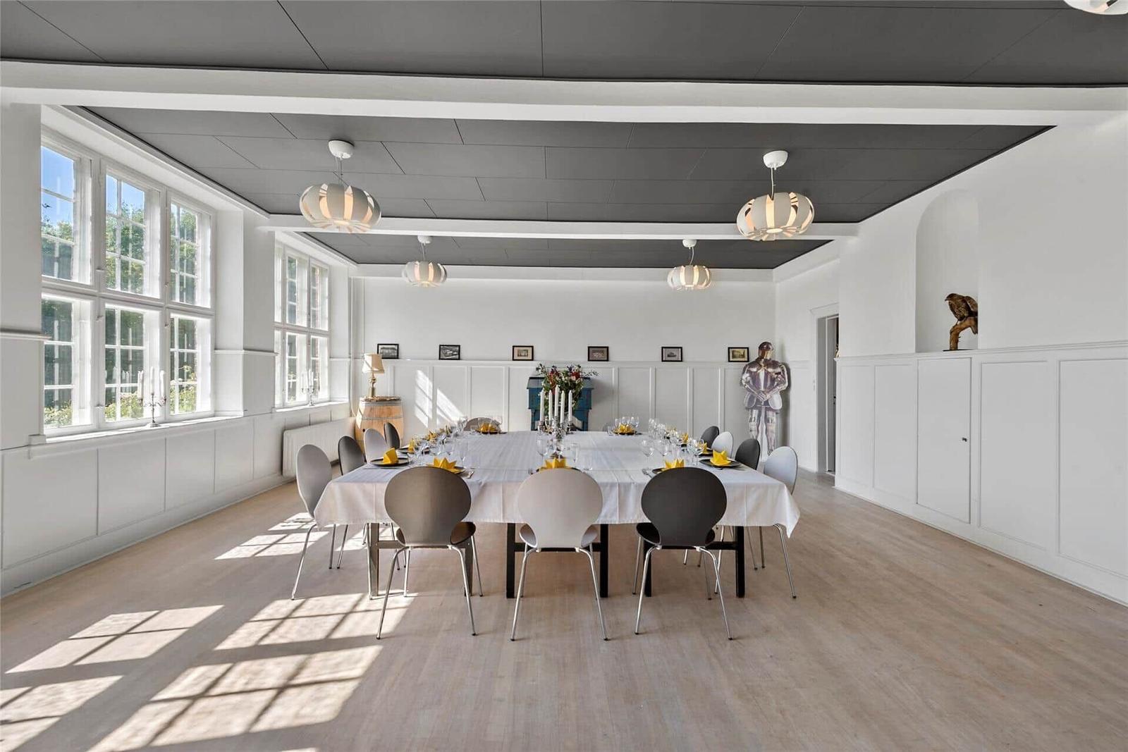 Großer Essraum mit Tisch, Stühlen und Fenstern. Decke mit Lampen und Wanddekoration.