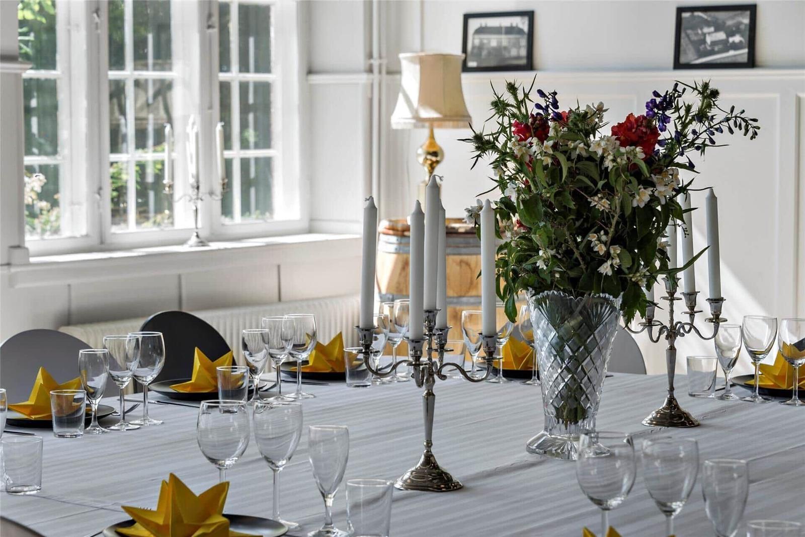 Gedeckter Tisch mit Blumen, Kerzen und Gläsern vor Fenster