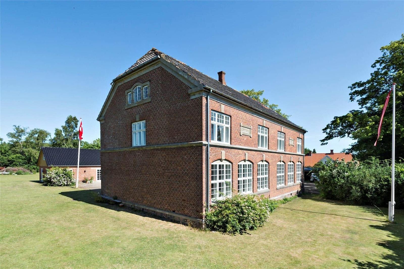 Rotes Backsteinhaus mit grünem Garten und Flagge. Mehrere Fenster und Dachgauben.