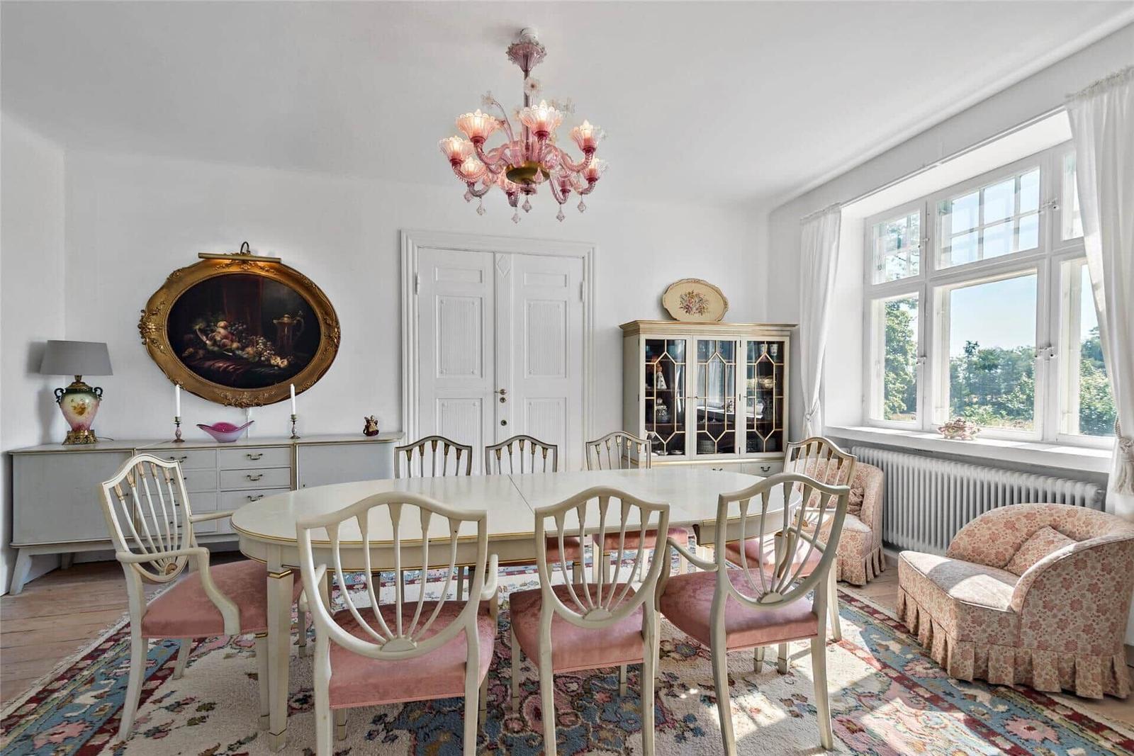 Esszimmer mit ovaler Tafel, Stühlen und Kronleuchter. Fenster mit Blick auf Garten.