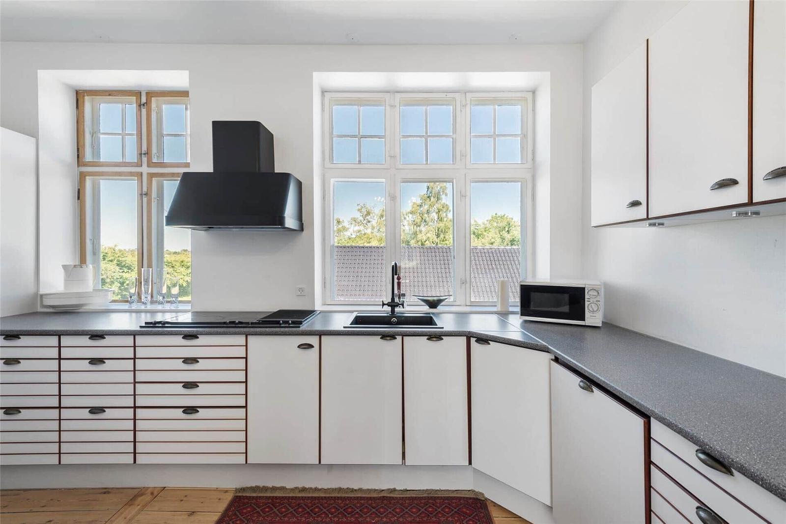 Küche mit weißen Schränken, dunklem Arbeitsplatz und großen Fenstern.