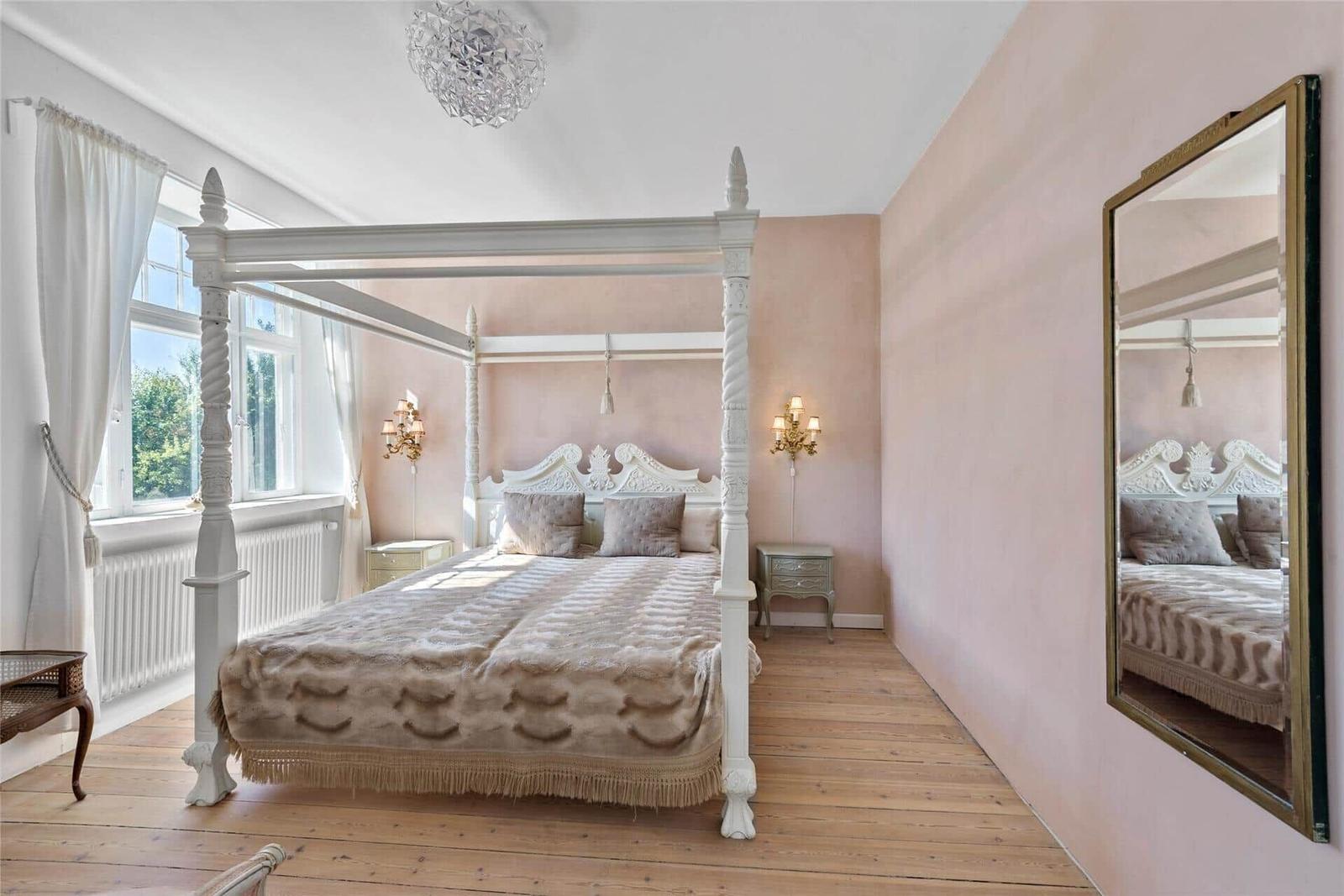 Schlafzimmer mit weißem Vierposterbett, Spiegel und Holzboden.