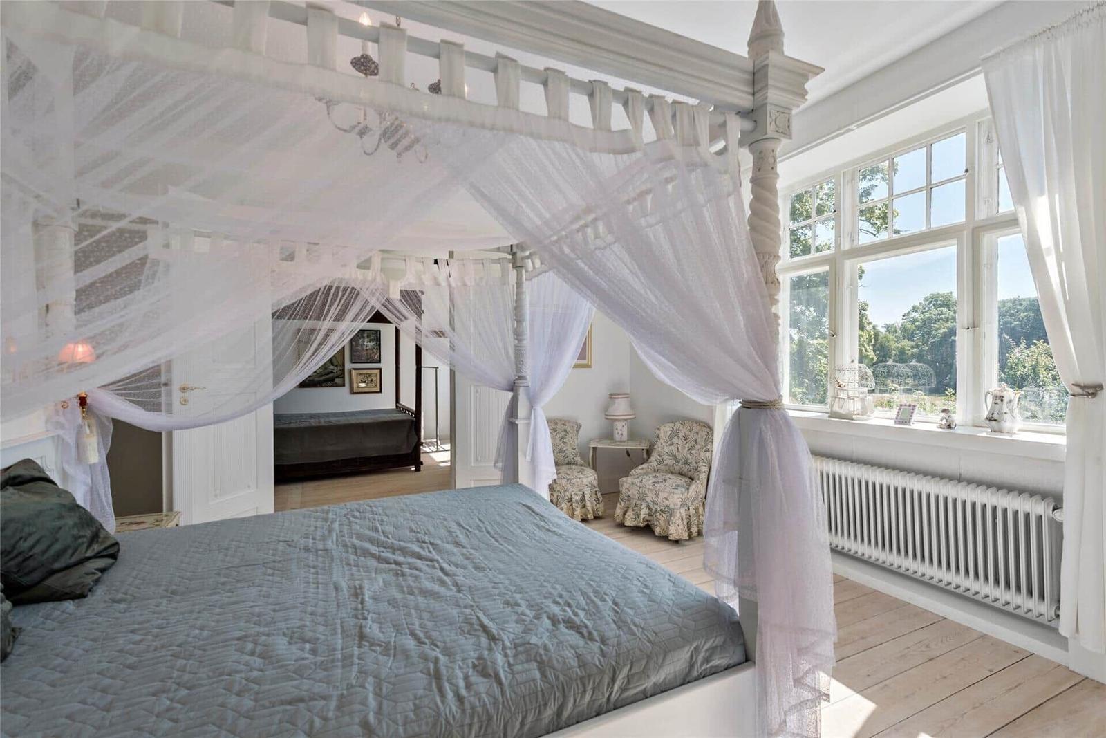 Schlafzimmer mit Baldachinbett, großen Fenstern und Holzboden.