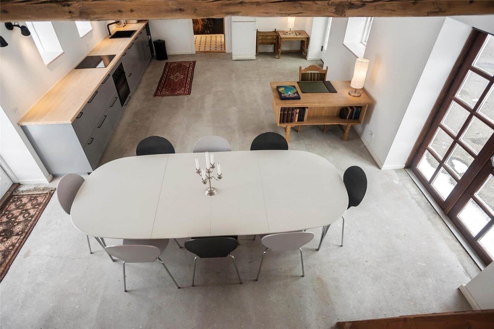 Esszimmer mit Tisch, Stühlen und Küchenbereich. Holzrahmen und Teppiche sichtbar.