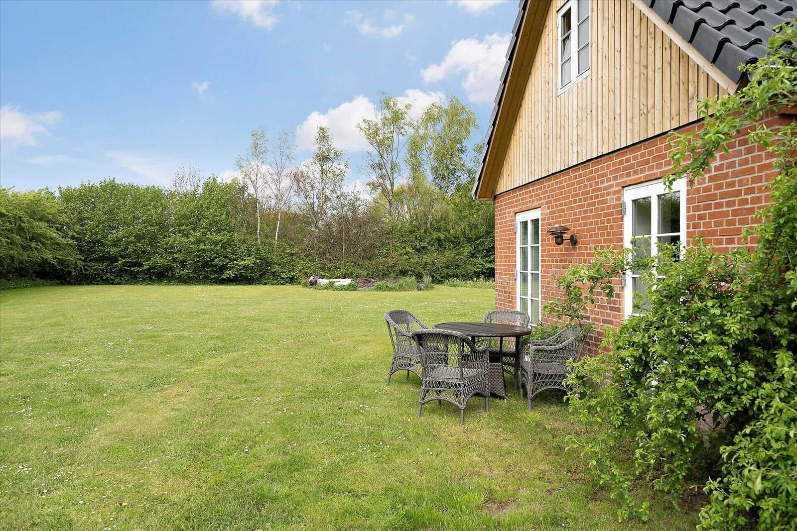 Haus mit Garten, Tisch und Stühlen, umgeben von Bäumen und Gras.