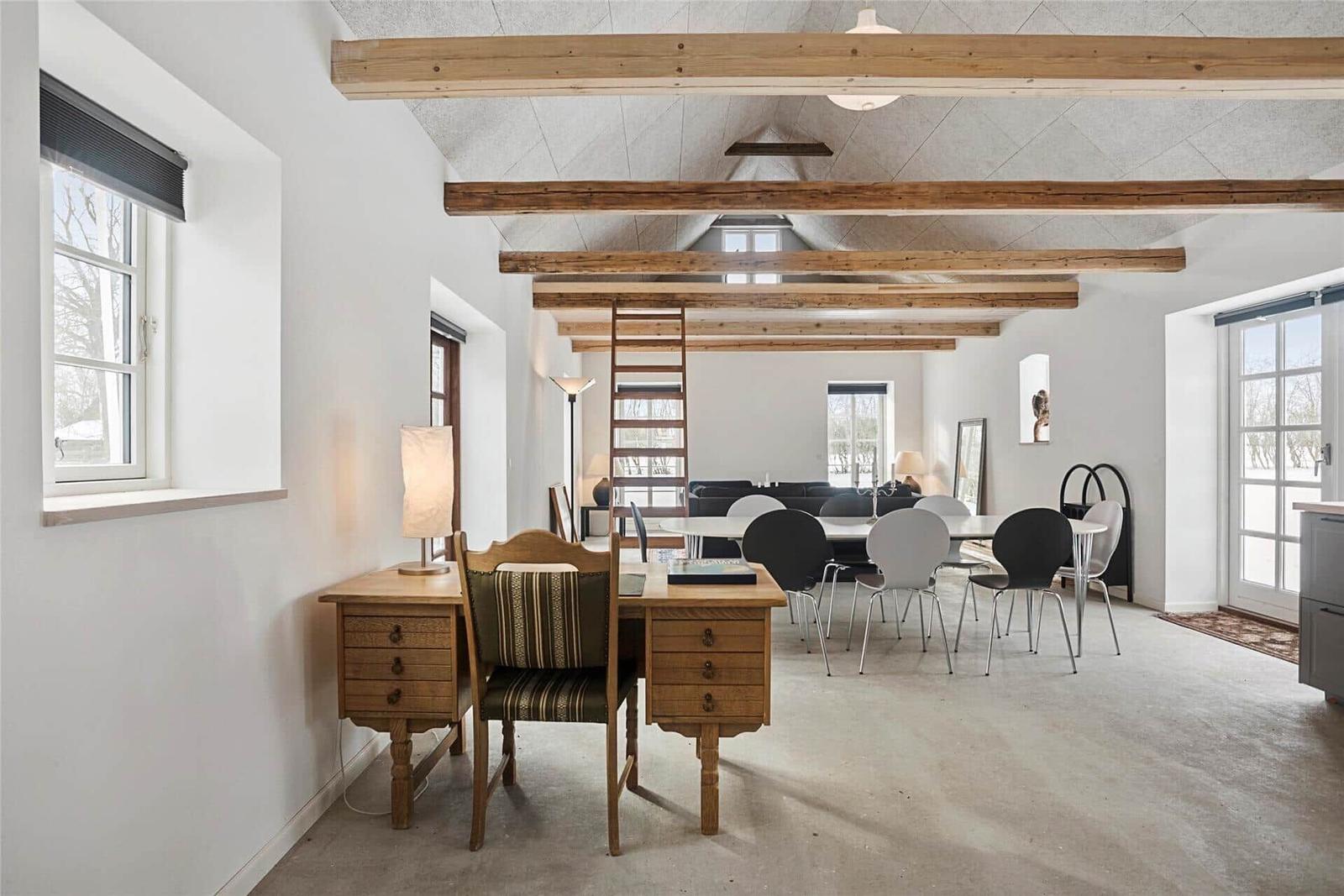 Großes Wohnzimmer mit Holzbalken, Schreibtisch und Essbereich. Fenster und Tür bieten viel Licht.