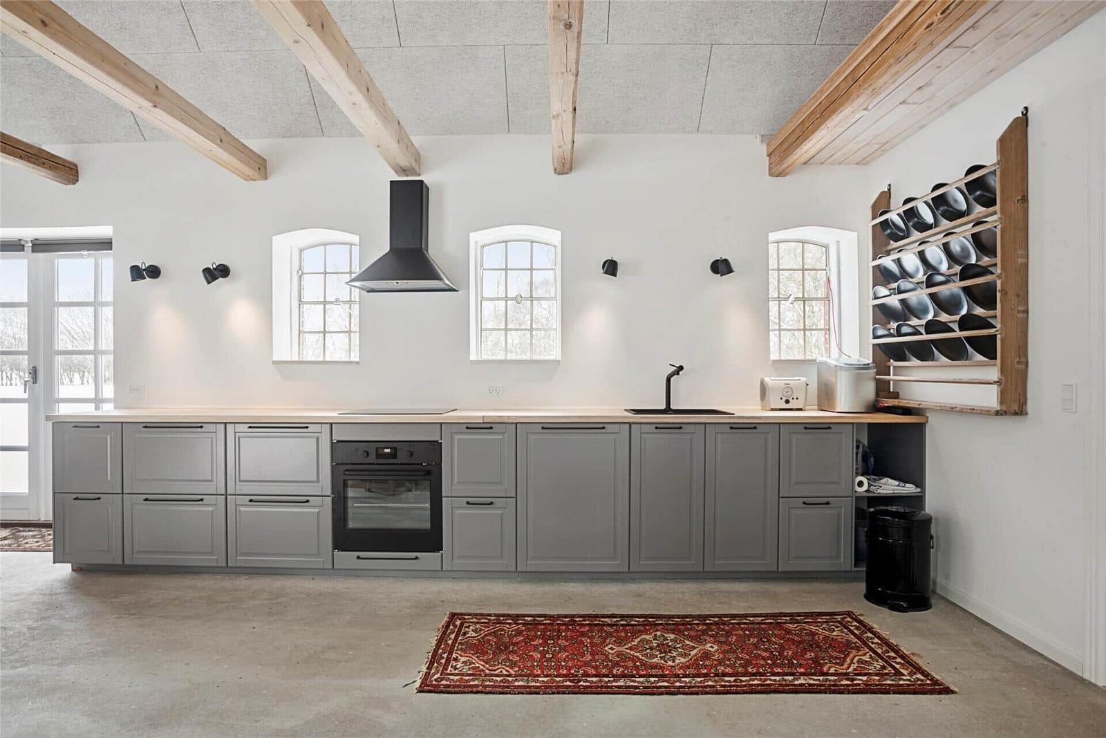 Küche mit grauen Schränken, rotem Teppich und Holzbalken an der Decke.