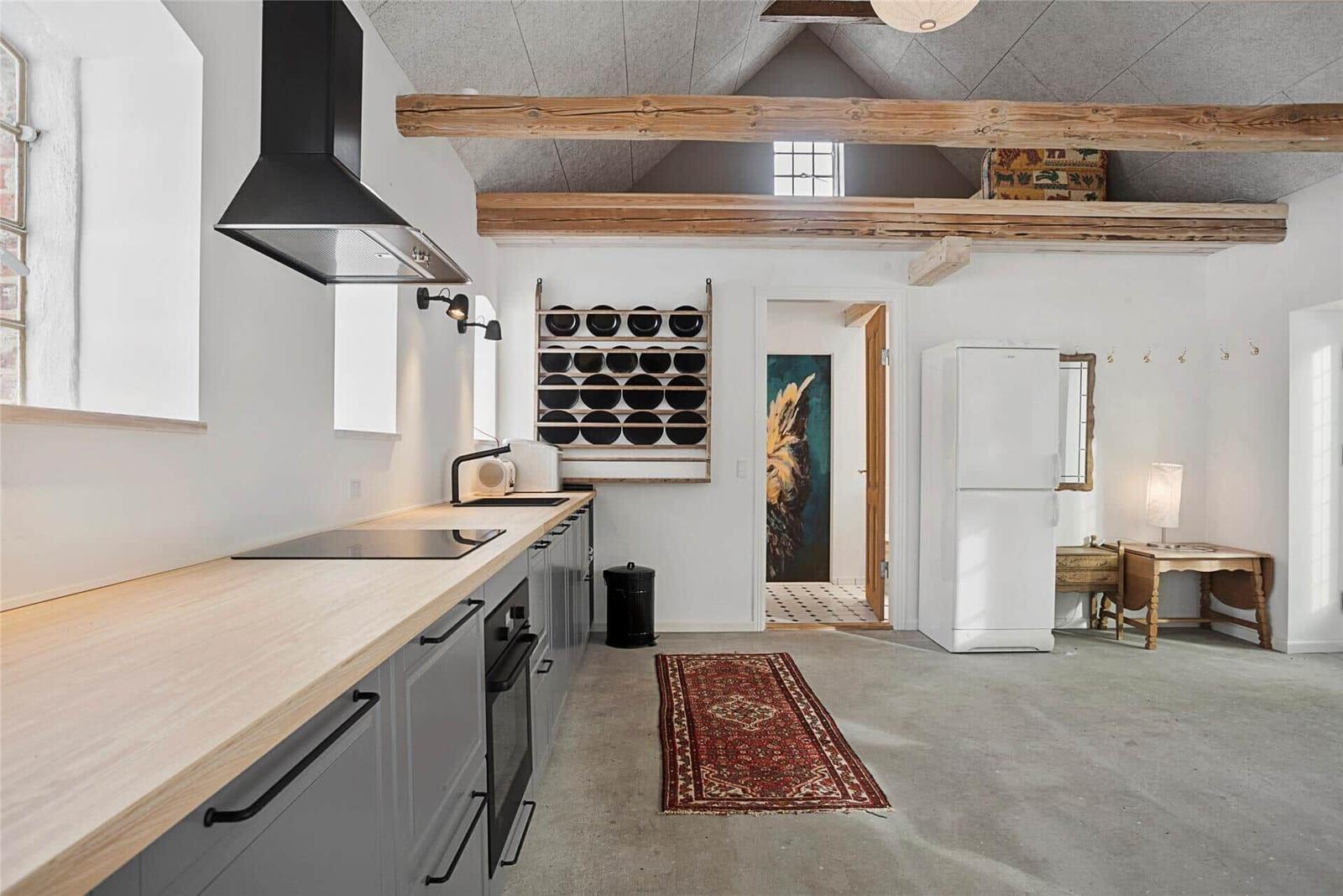 Küche mit Holzplatte, Kühlschrank und rotem Teppich unter Holzbalken.