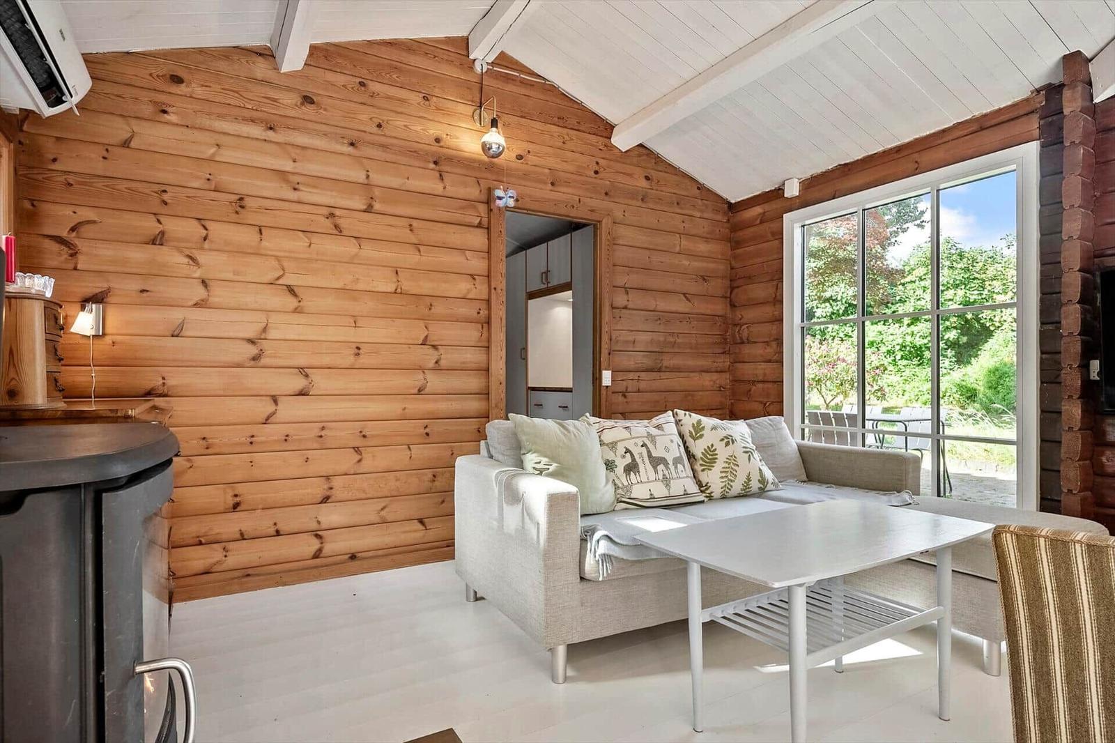 Wohnzimmer mit Holzwand, Sofa und Tisch. Durchgang zur Küche. Fenster zur Terrasse.