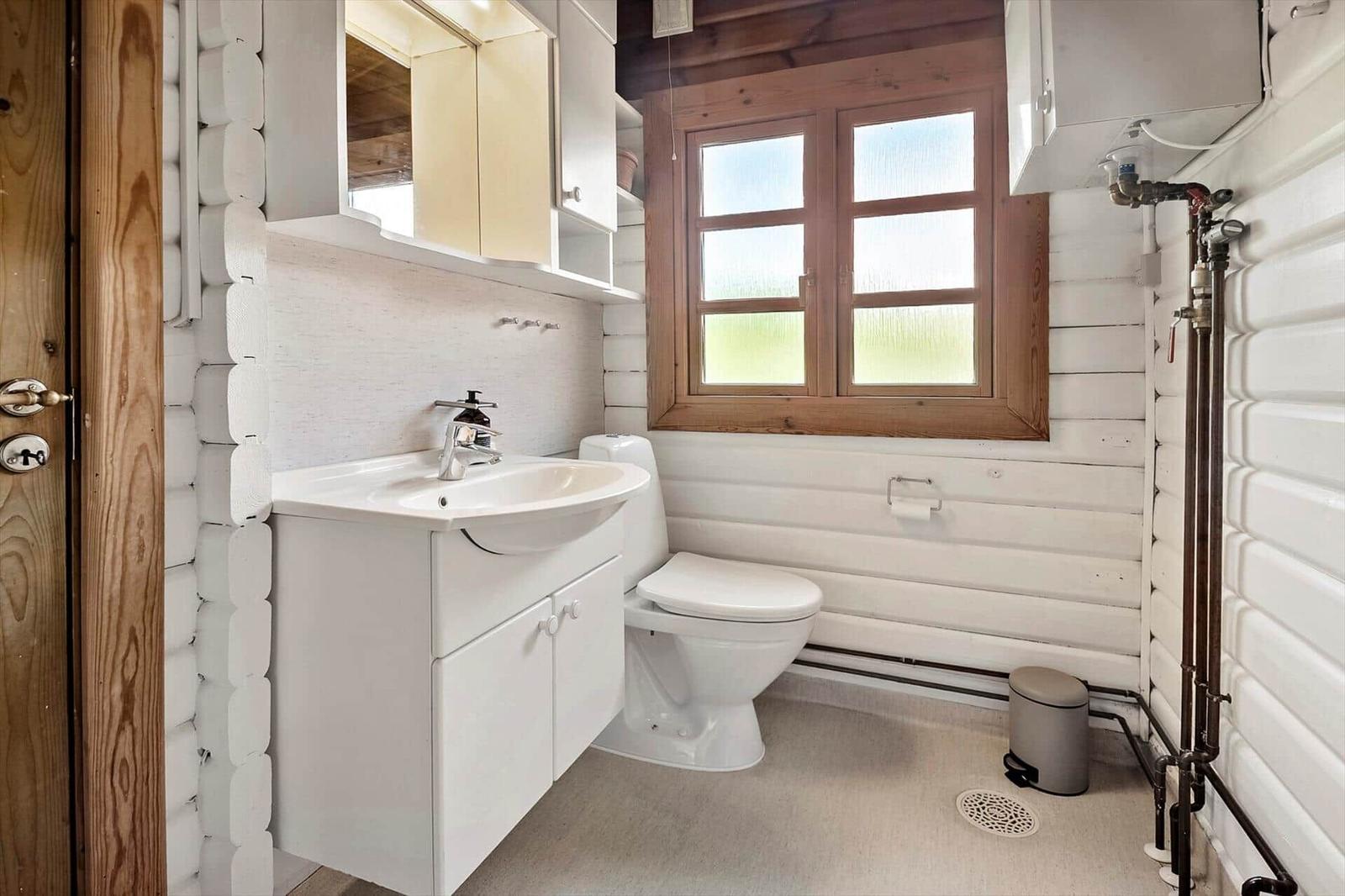 Badezimmer mit Waschbecken, Toilette und Fenster. Wände aus Holz und weiße Möbel.