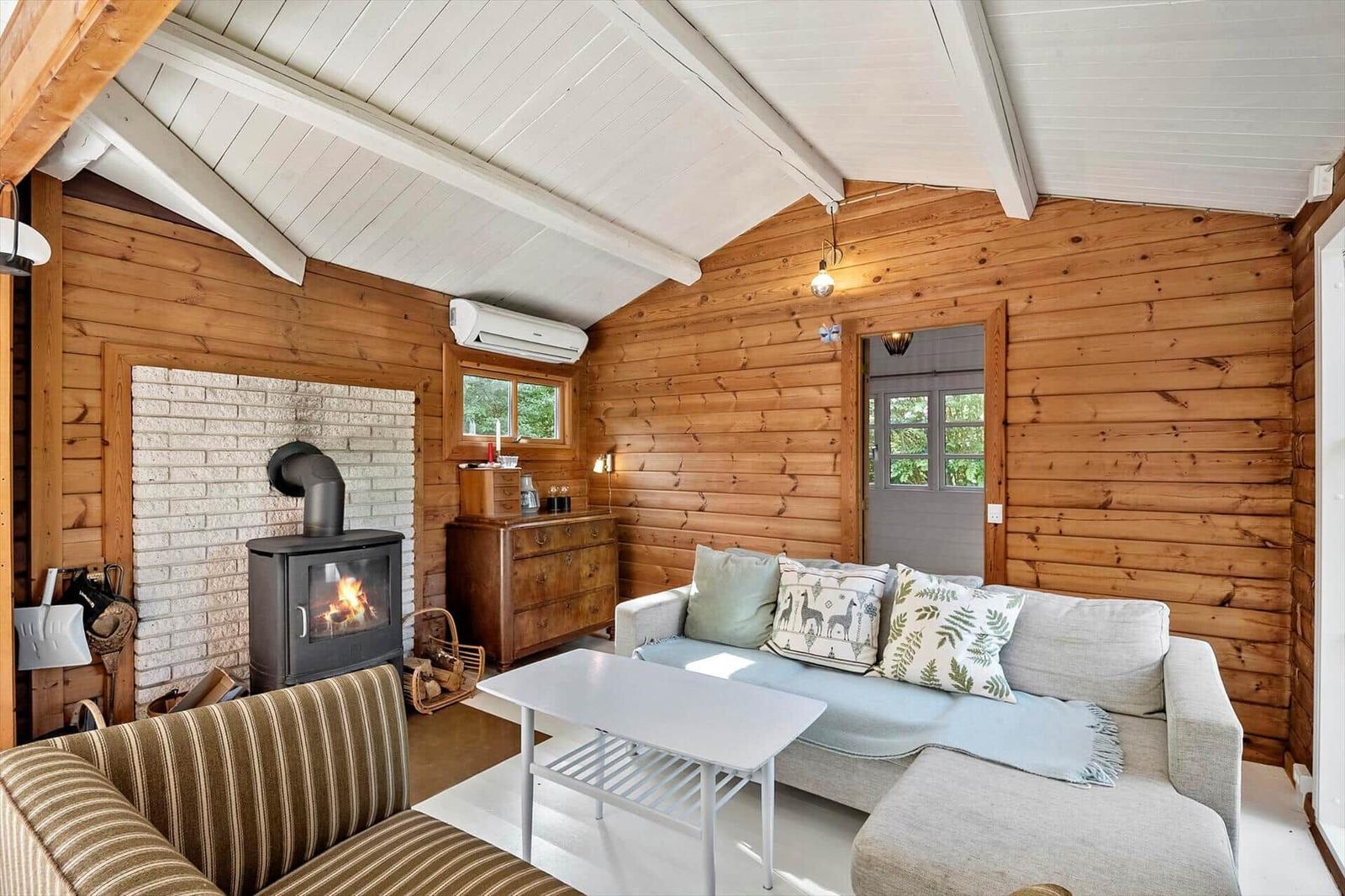 Wohnzimmer mit Kamin, Sofa und Holzwand. Fenster und Tür zeigen Grün.
