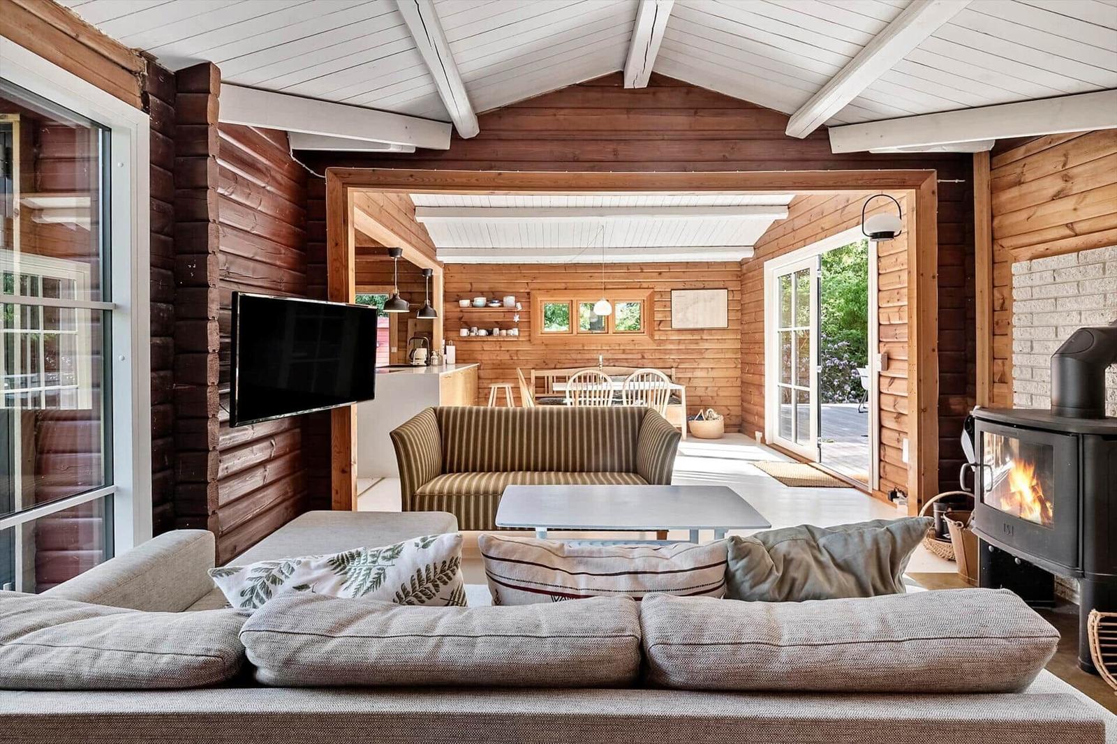 Wohnzimmer mit Kamin, Sofa und Fernseher. Durchgang zur Küche und Terrasse.