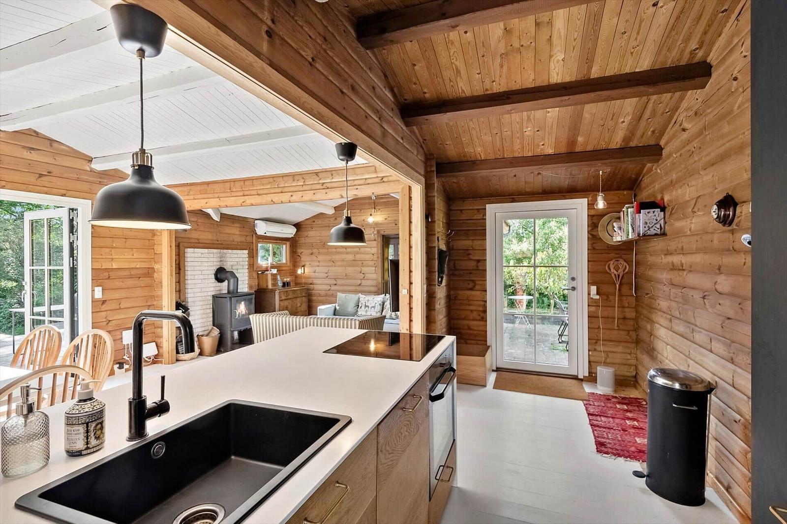 Küche mit Arbeitsplatte, Spüle und Dunstabzug. Holzwände und Deckenbalken. Tür zum Garten.