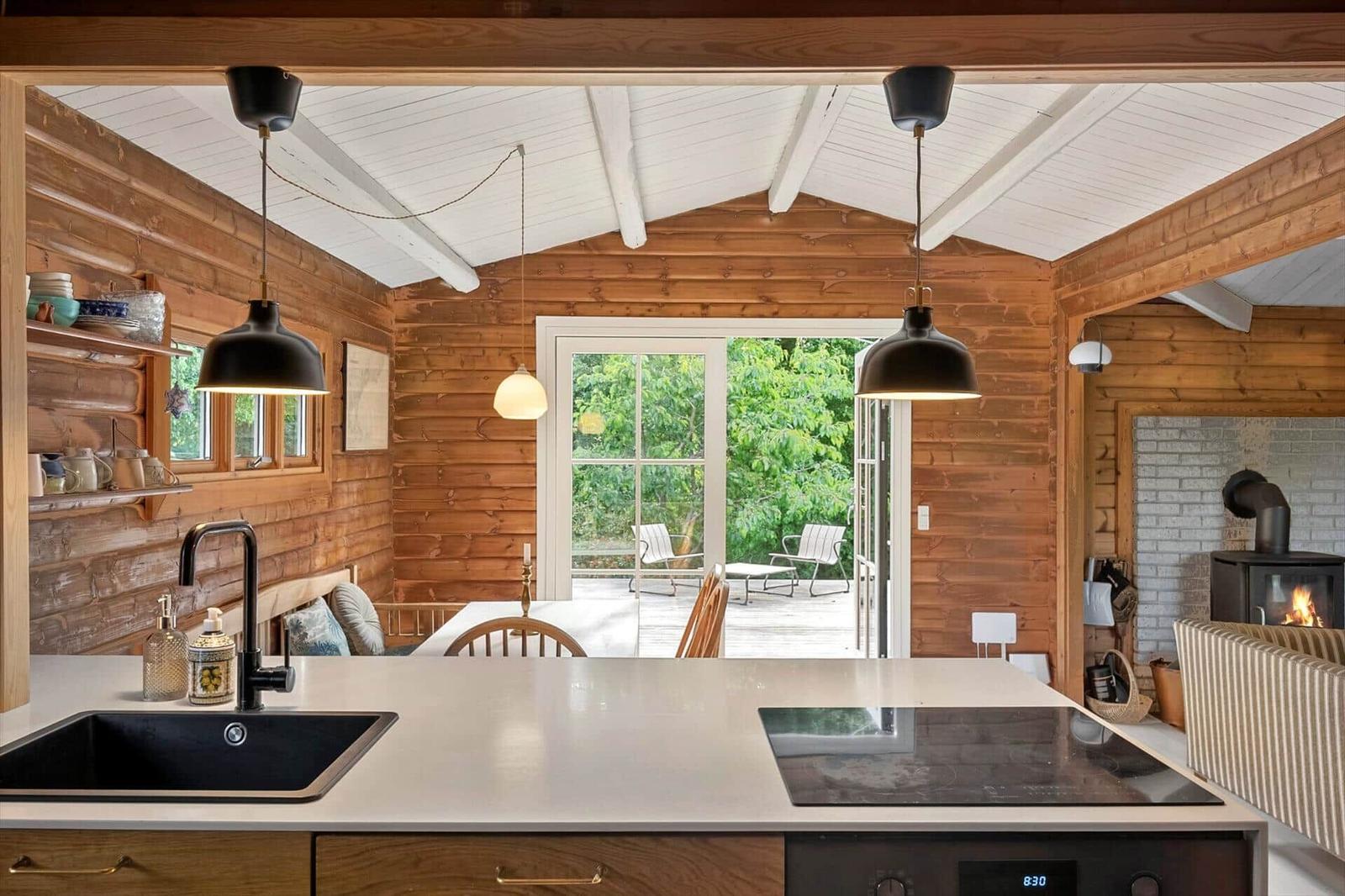 Küche mit Holzwand und Fenster zur Terrasse. Kamin und Kochfeld sind sichtbar.
