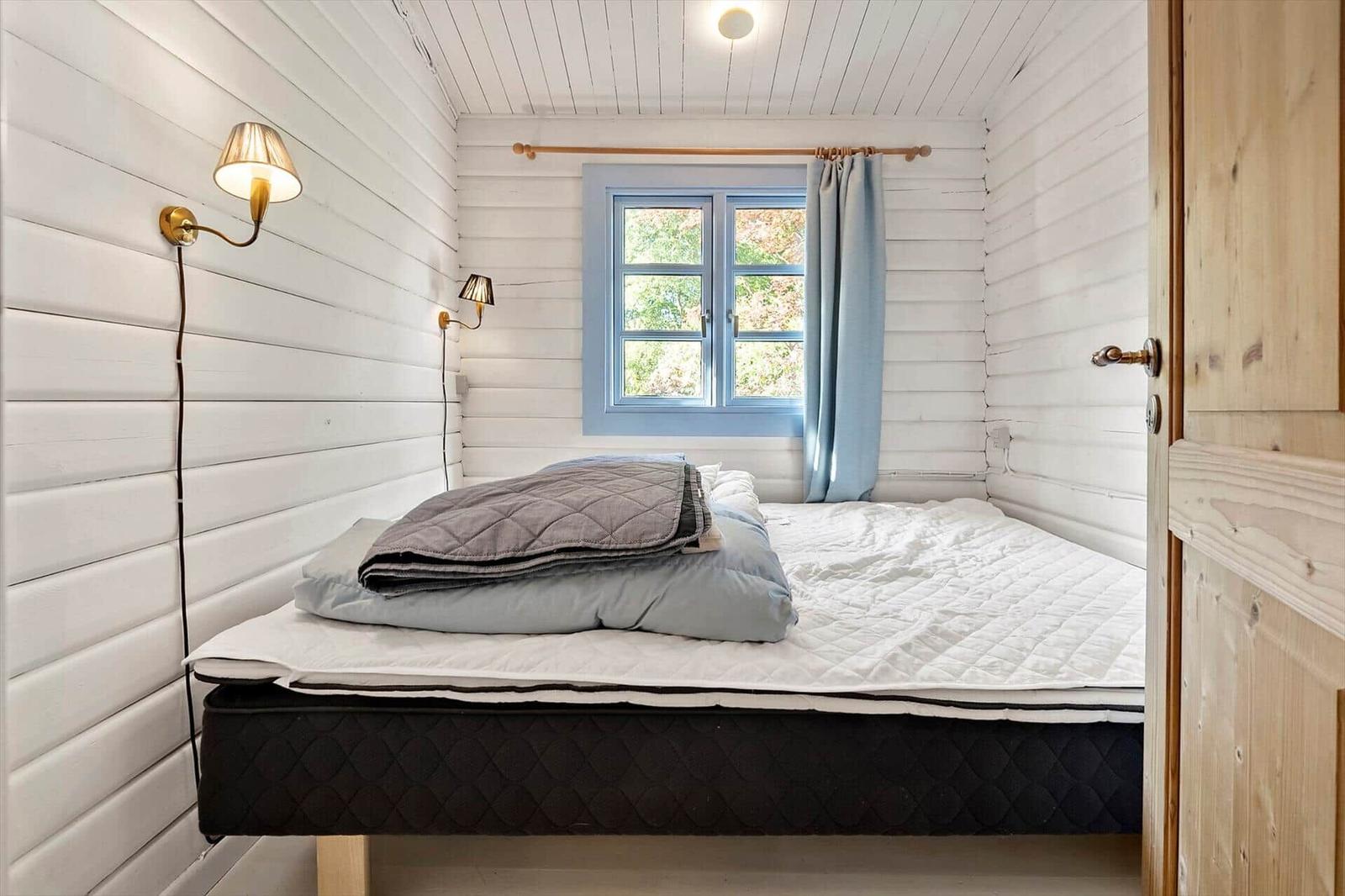 Schlafzimmer mit Bett, Fenster und Wandlampen in weißer Holzwand.