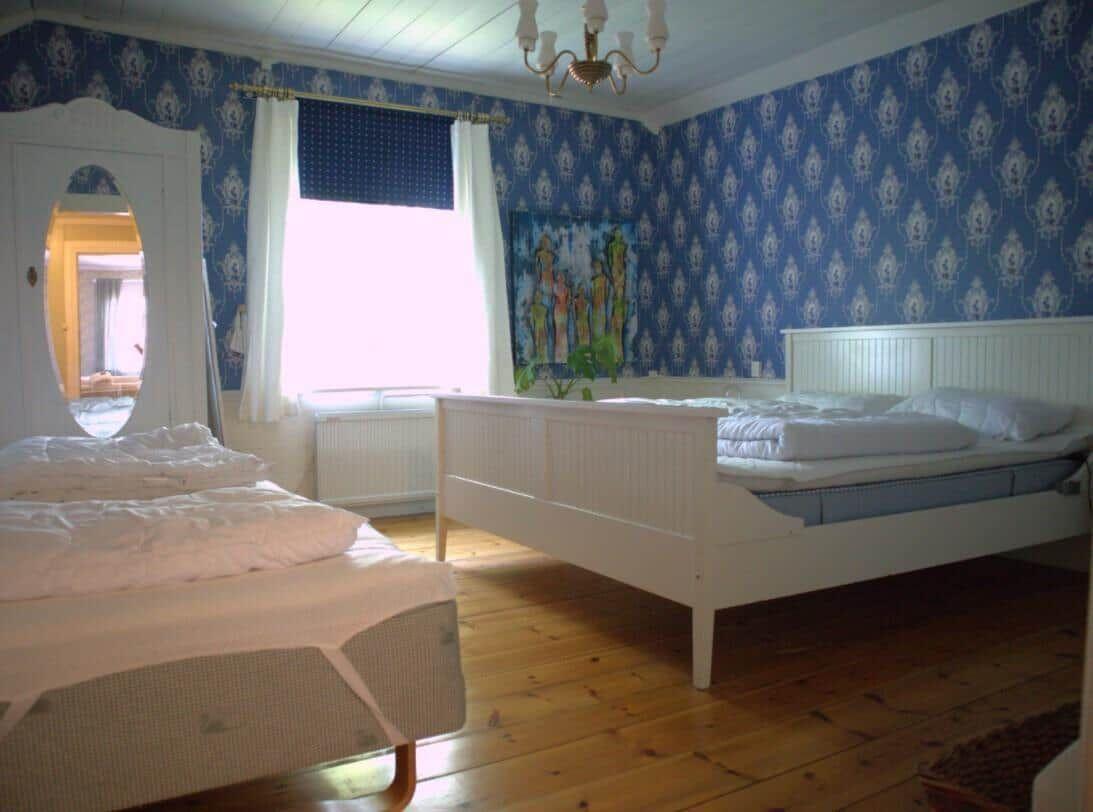 Zwei Betten mit weißen Laken, blaue Tapete und Holzboden im Schlafzimmer.
