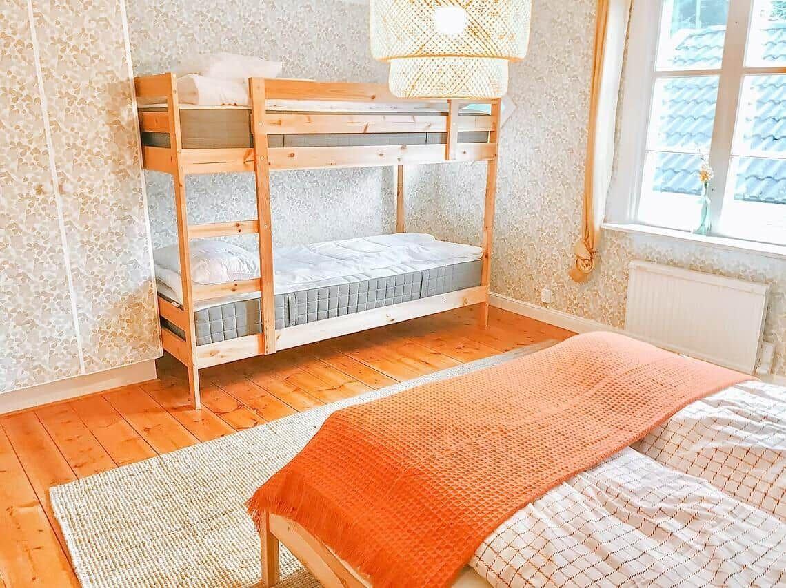 Zimmer mit Doppelstockbett und Einzelbett, Holzboden und Fenster mit Blick.