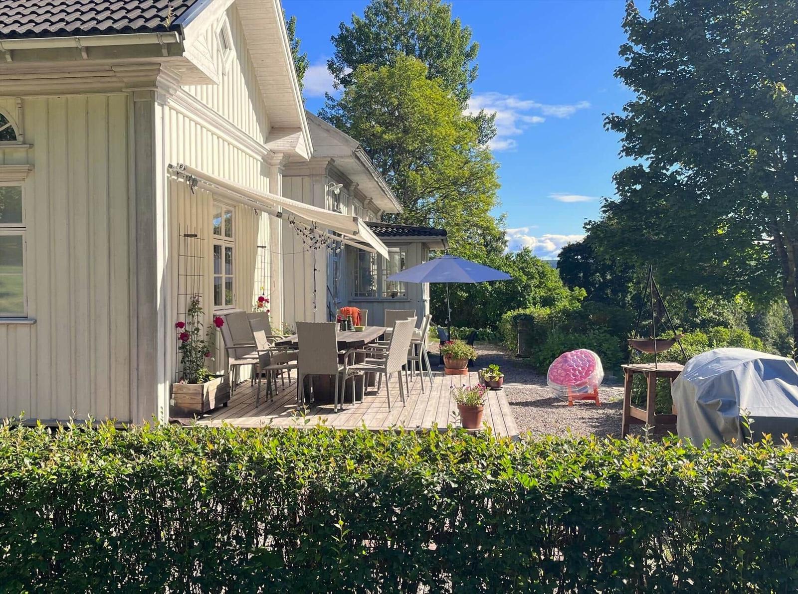 Terrasse mit Tisch, Stühlen und Sonnenschirm neben einem Haus mit Balkon.
