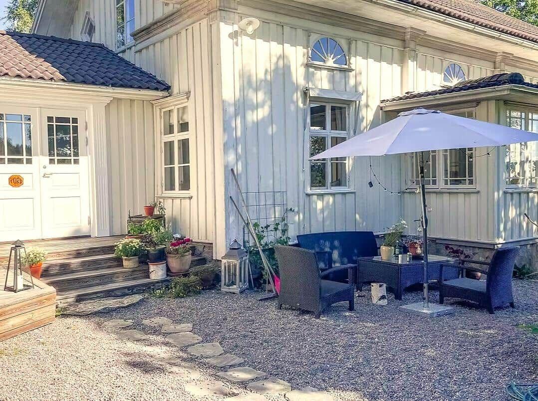 Haus mit Terrasse, Sitzgruppe und Sonnenschirm. Pflanzen und Steine dekorieren den Außenbereich.