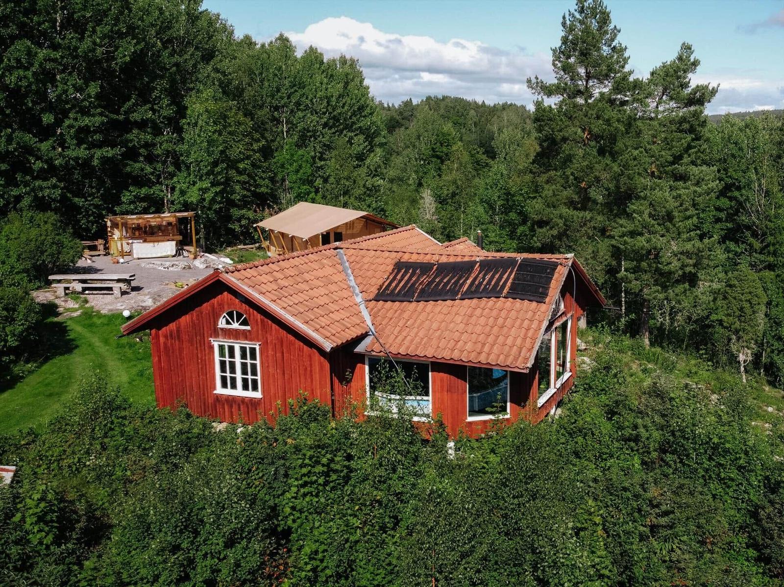 Rotes Holzhaus mit Solaranlage, umgeben von Wald und Grünfläche.