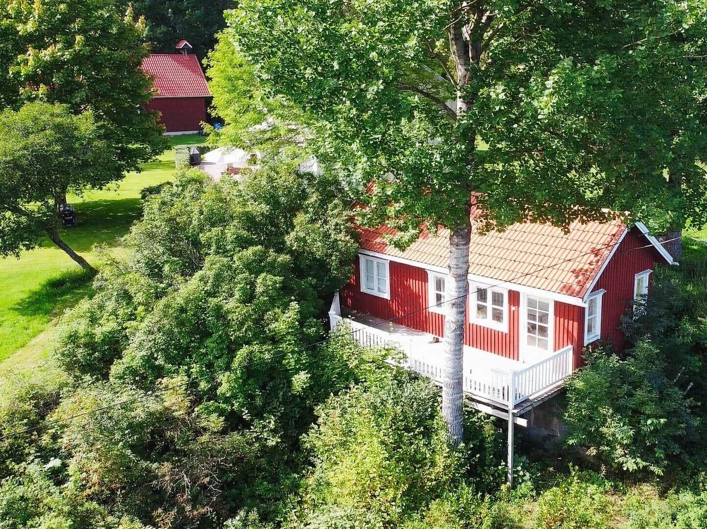 Rotes Haus mit weißen Fenstern und Veranda, umgeben von grünen Bäumen und Rasen.