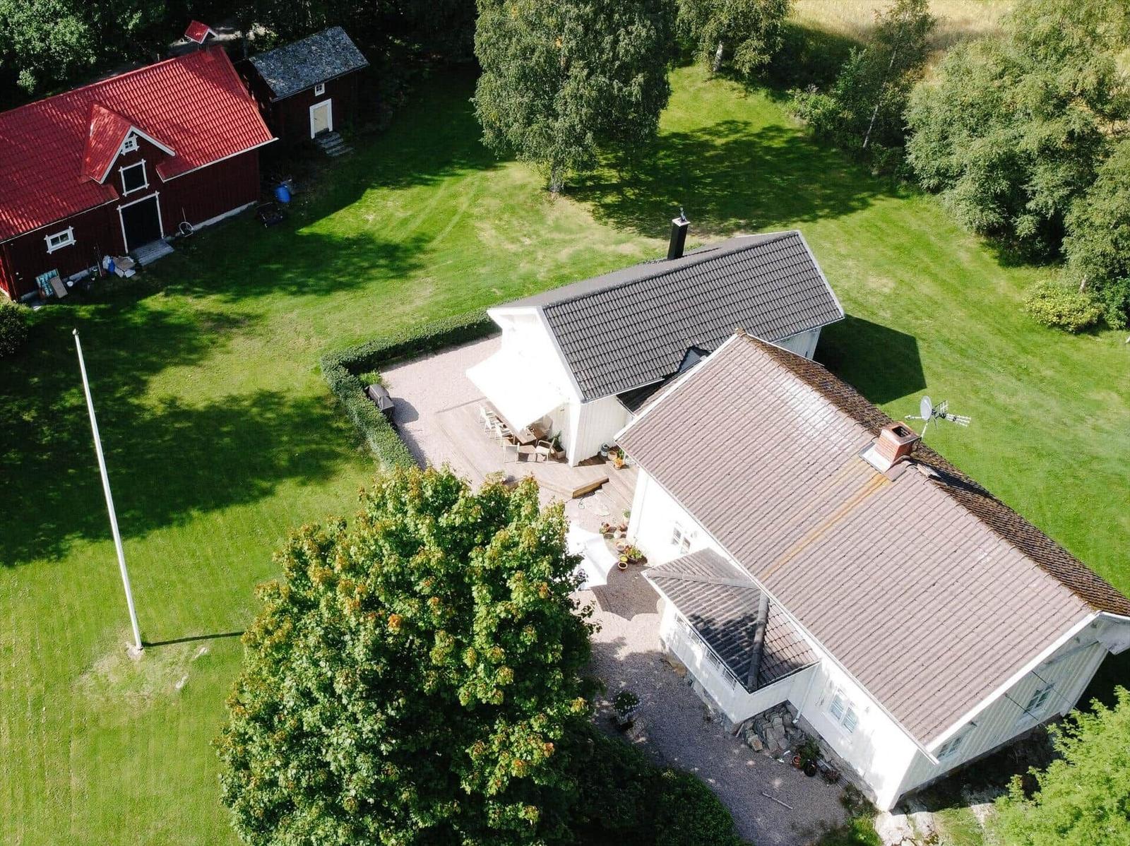 Haus mit Garten, Terrasse und rotem Schuppen. Umgeben von Bäumen und Gras.
