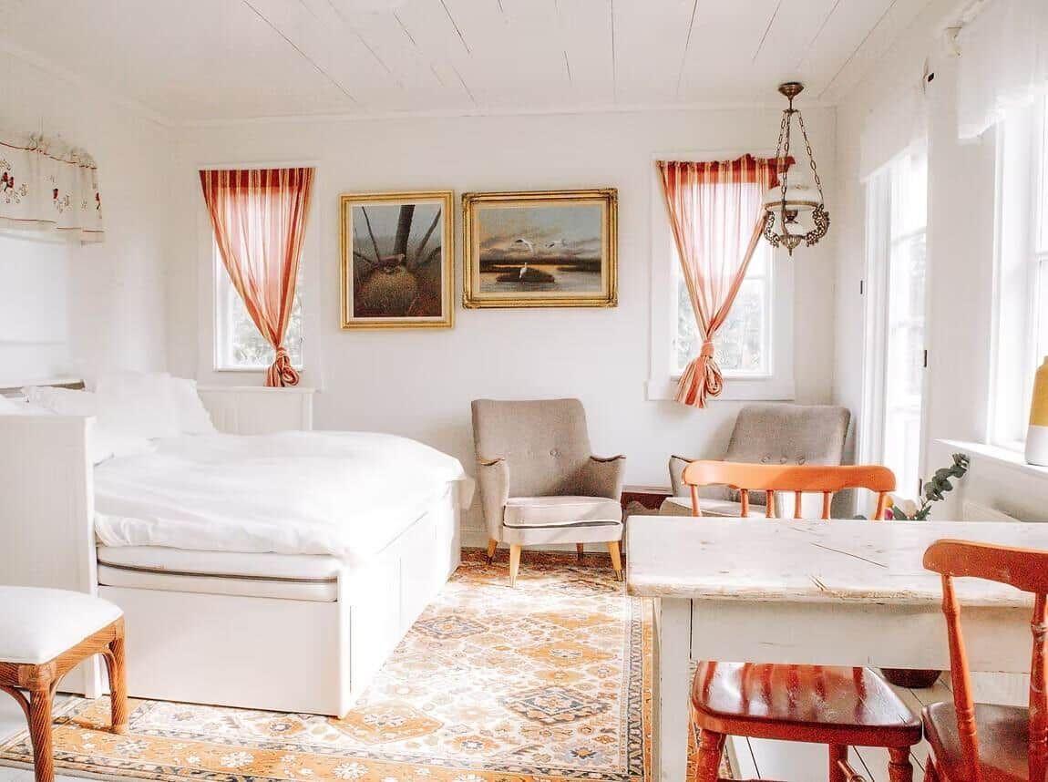 Ein Schlafzimmer mit Bett, Stühlen und Wandbildern. Fenster mit roten Vorhängen.