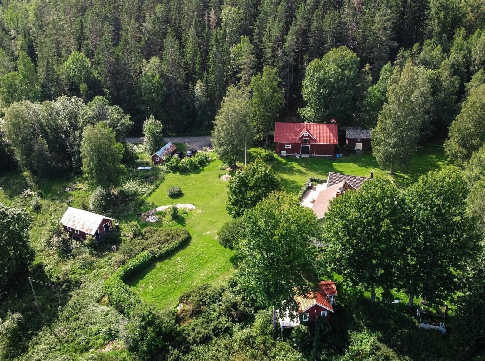 Roter Holzhauskomplex mit Grünfläche und Wald im Hintergrund.