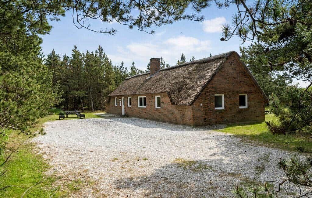 Haus mit Strohdach, umgeben von Bäumen und Grasfläche.