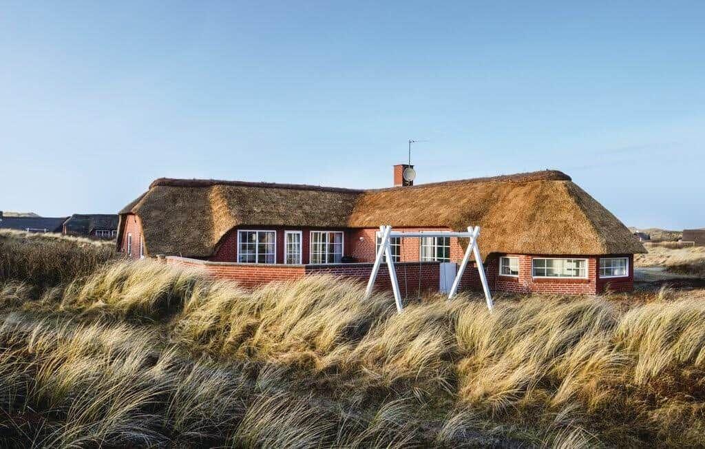 Rotes Backsteinhaus mit strohgedecktem Dach, umgeben von hohem Gras.