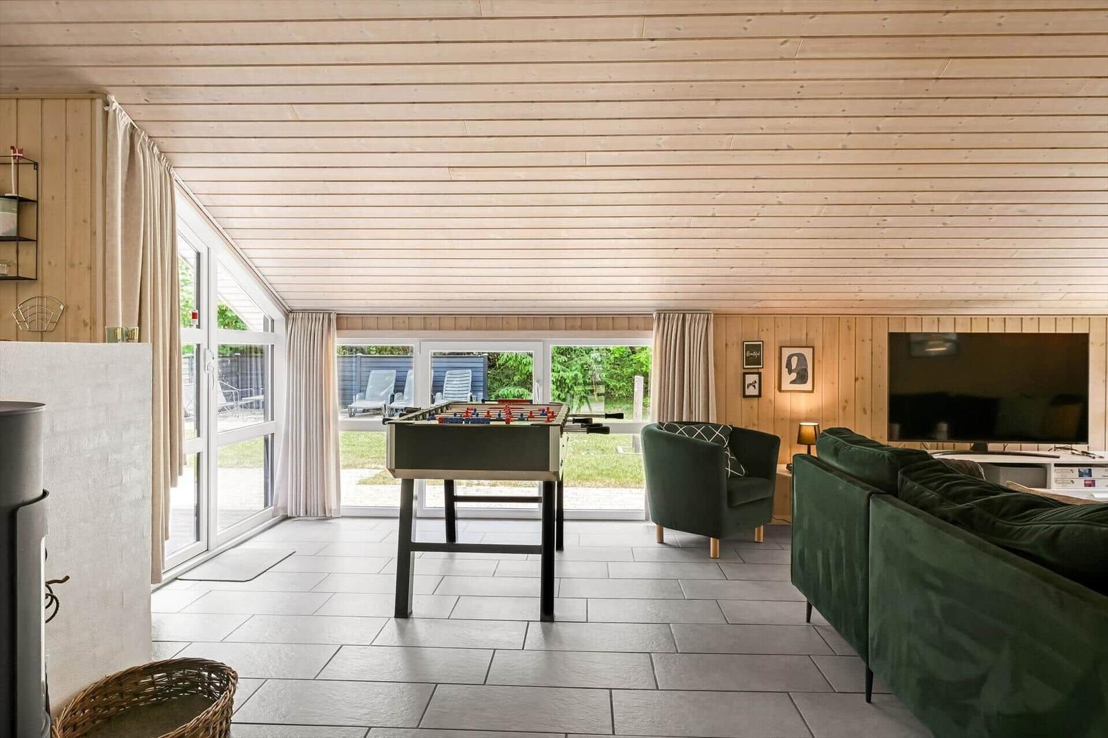 Wohnraum mit Tischfußball, Sofa und Fernseher. Holzdecke und große Fenster.