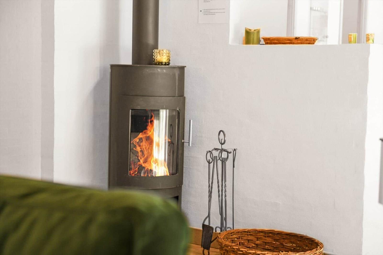 Ein Kaminofen mit brennendem Feuer, daneben steht ein Feuerzeughalter und ein Korb.