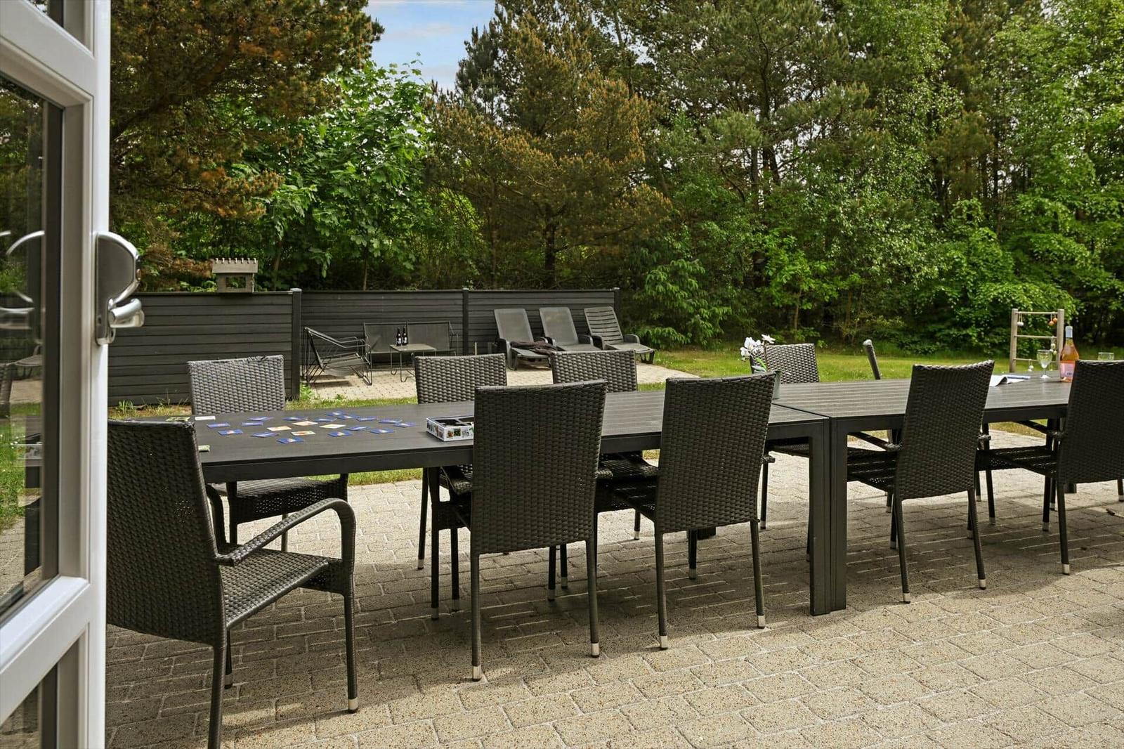 Terrasse mit Esstisch und Stühlen, umgeben von Grünfläche und Bäumen.