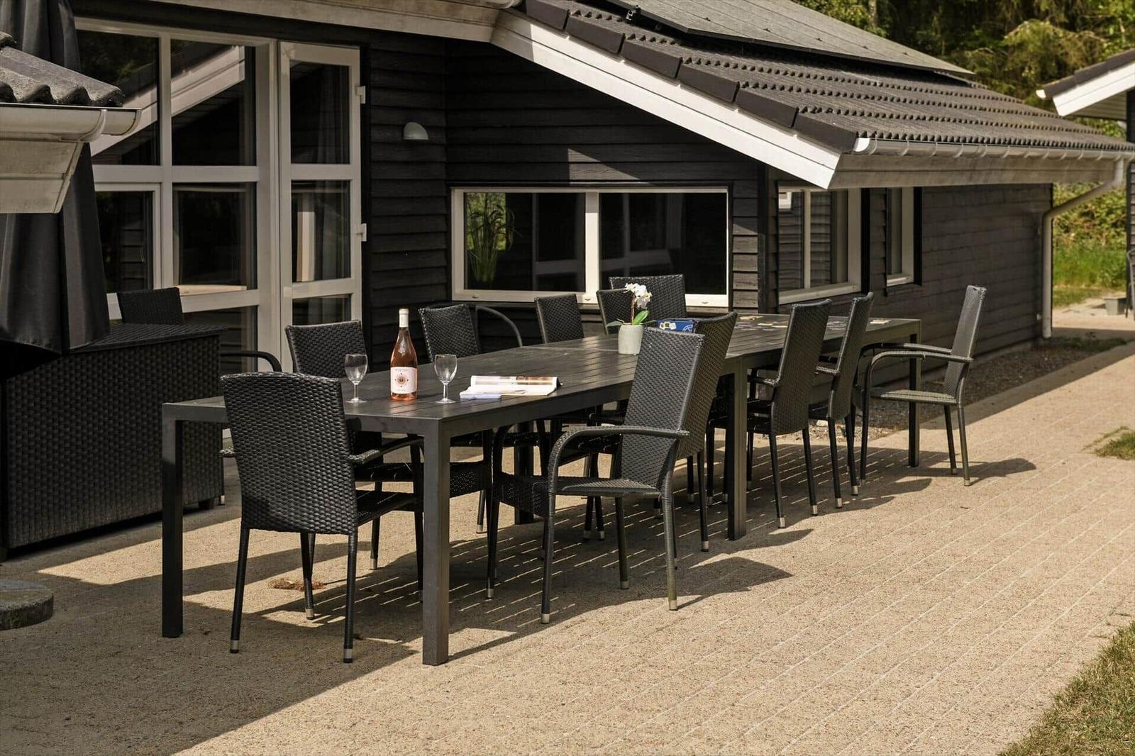 Terrasse mit Tisch und Stühlen vor einem Haus mit dunklem Holzschindelverkleidung.