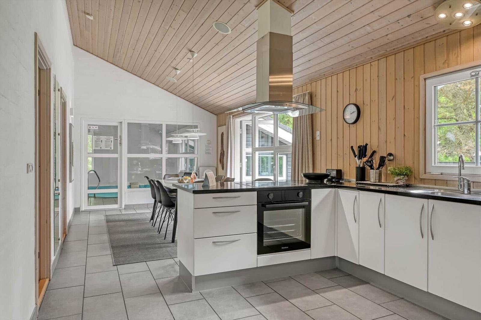Küche mit weißer Arbeitsplatte und Edelstahlherd. Holzwände und -decke. Blick in Essbereich mit Pool.