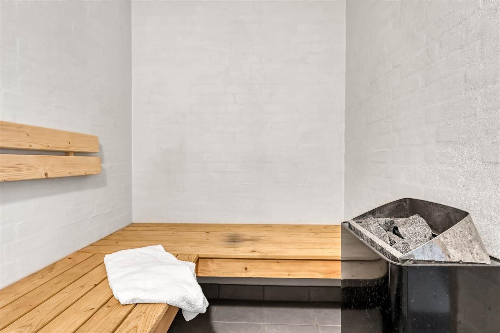 Sauna mit Holzbank und Steinkasten. Weiße Wände und gefaltete Handtuch.