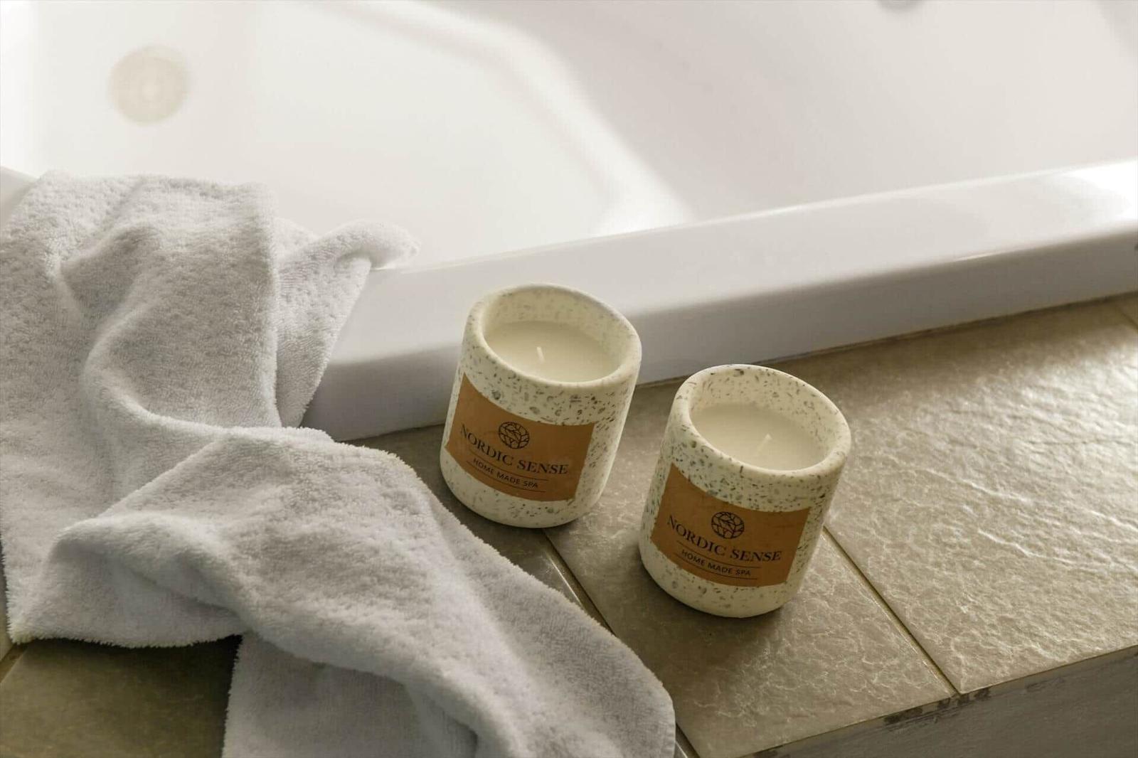 Zwei Kerzen und ein Handtuch neben einer Badewanne.