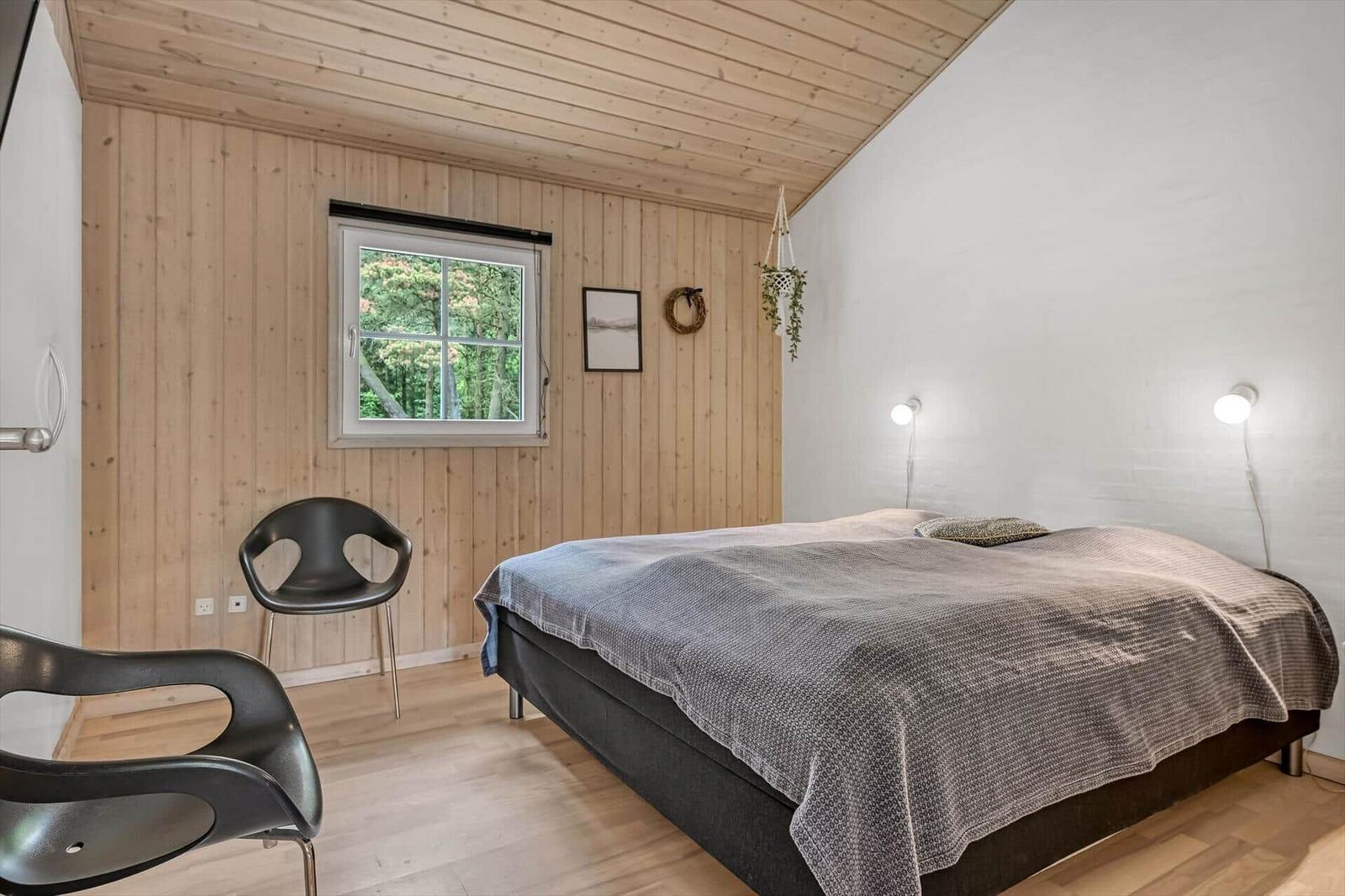 Schlafzimmer mit Bett, Fenster und zwei Stühlen. Holzwand und Decke.