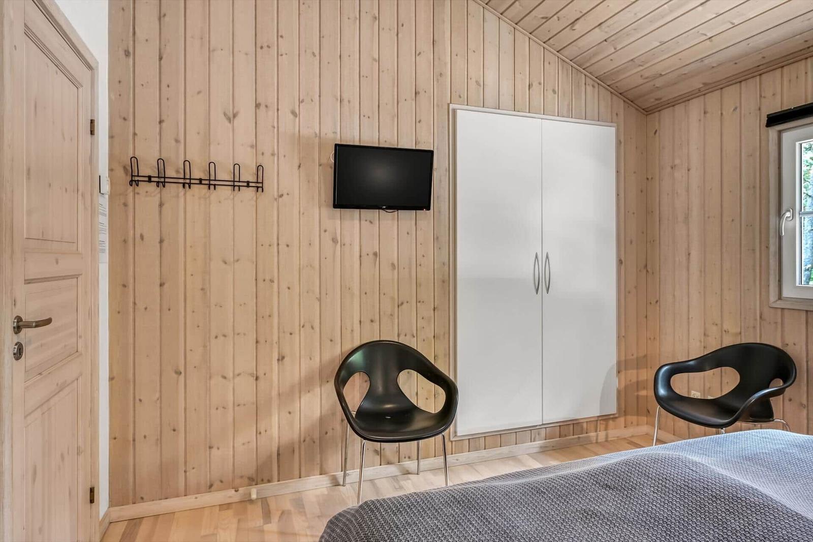 Schlafzimmer mit Holzwand, Bett, Kleiderschrank, TV und zwei Stühlen.