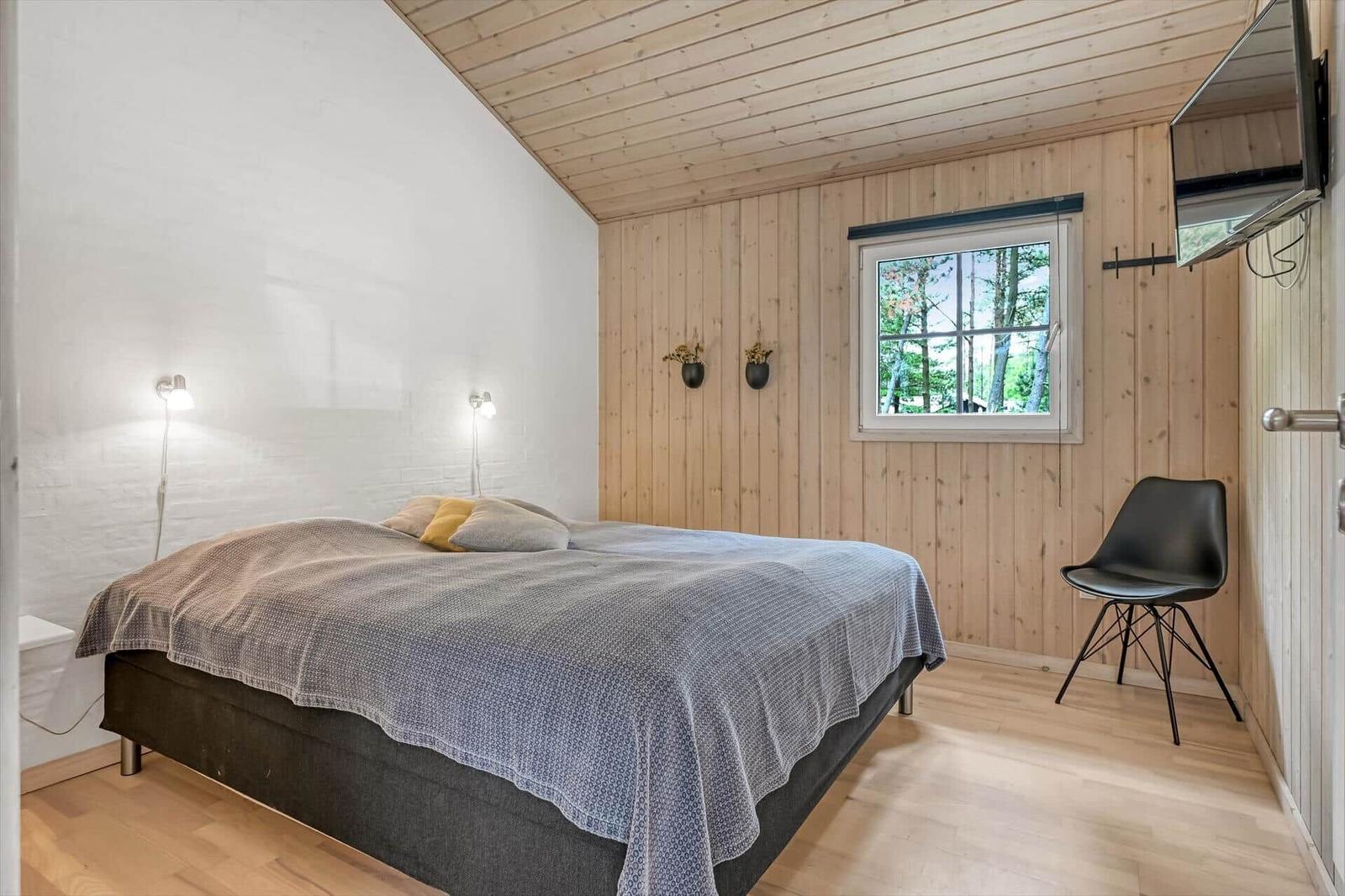Schlafzimmer mit Bett, Fenster und Stuhl. Holzwände und Decke.
