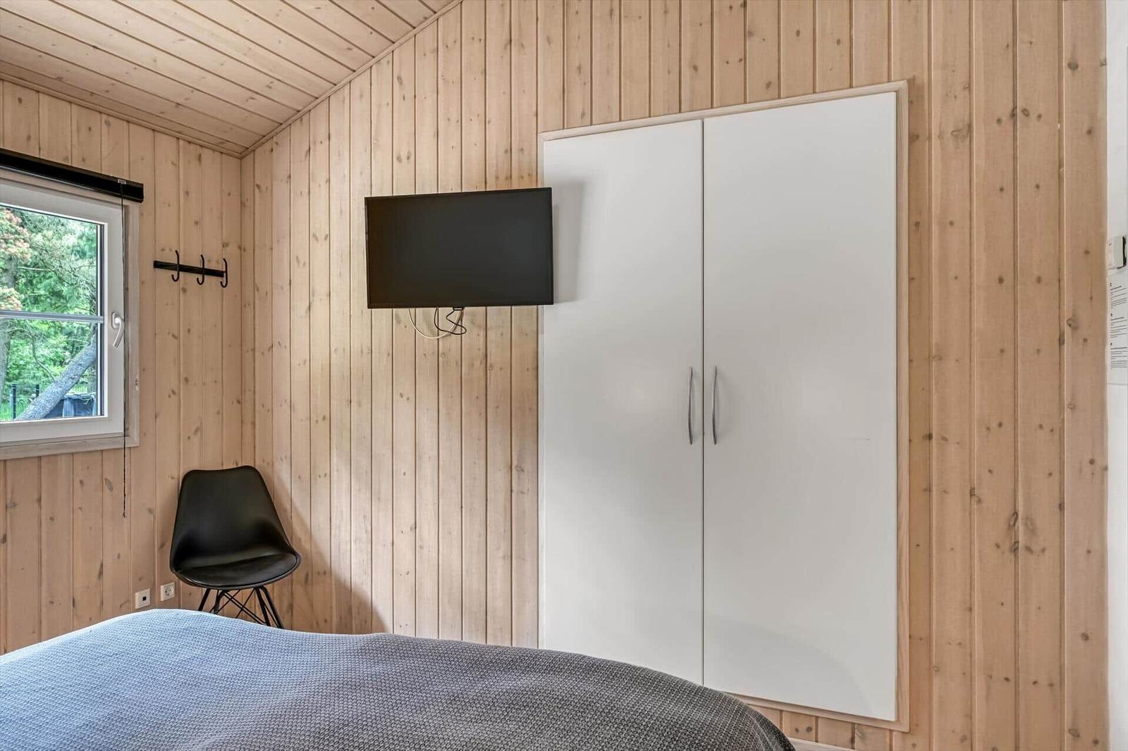 Schlafzimmer mit Holzwand, Bett, KleiderSchrank, TV und Stuhl.