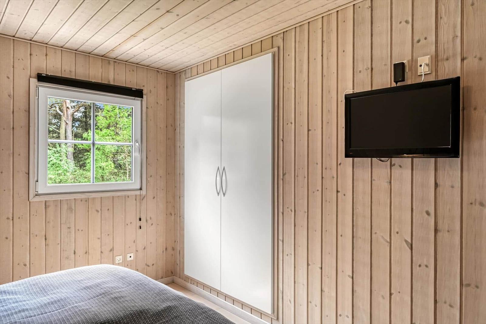 Schlafzimmer mit Holzwand, Fenster, Kleiderschrank und Wandfernseher.