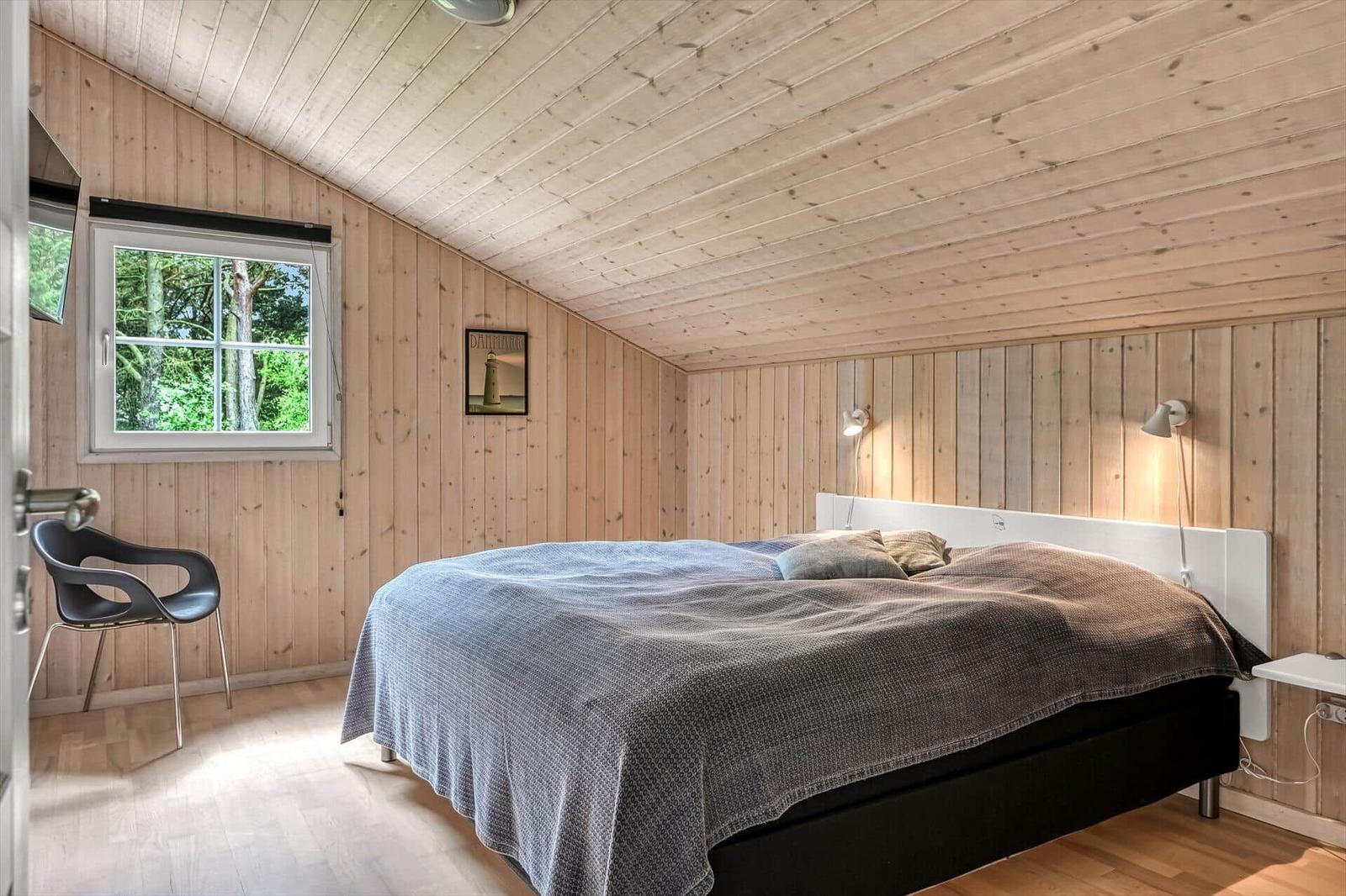 Schlafzimmer mit Holzwand, Bett, Fenster und Stuhl