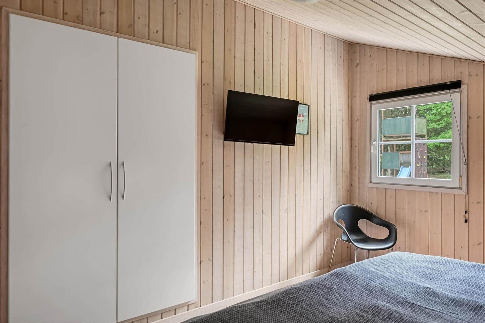 Schlafzimmer mit Bett, Kleiderschrank, TV und Fenster zum Garten.
